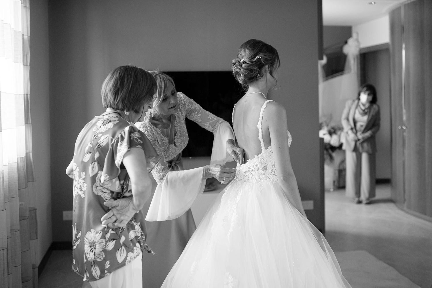 Final wedding dress adjustments being made in a hallway before the ceremony.