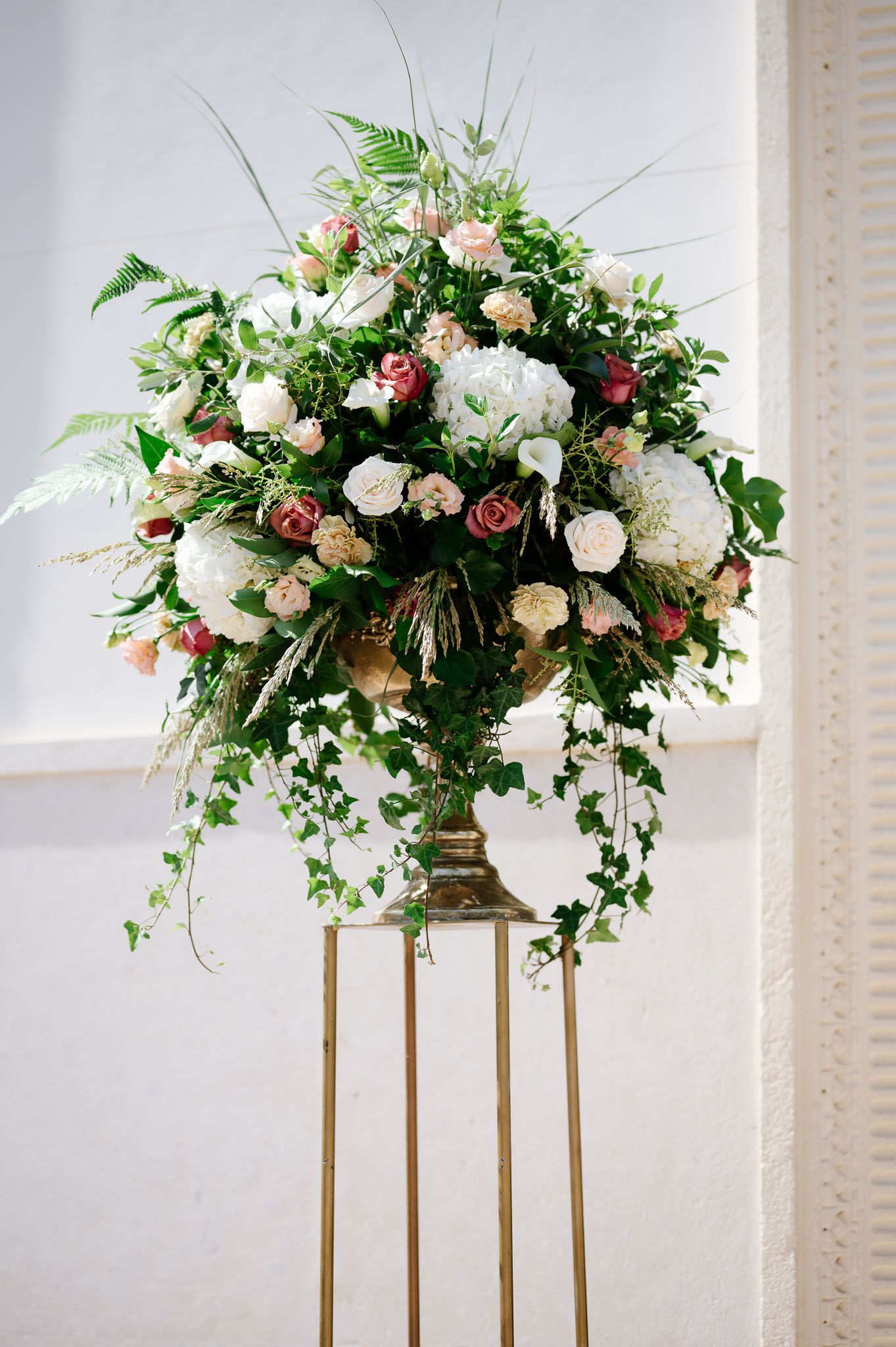 Elegant floral arrangement with white and pink roses on a gold stand against a light background.