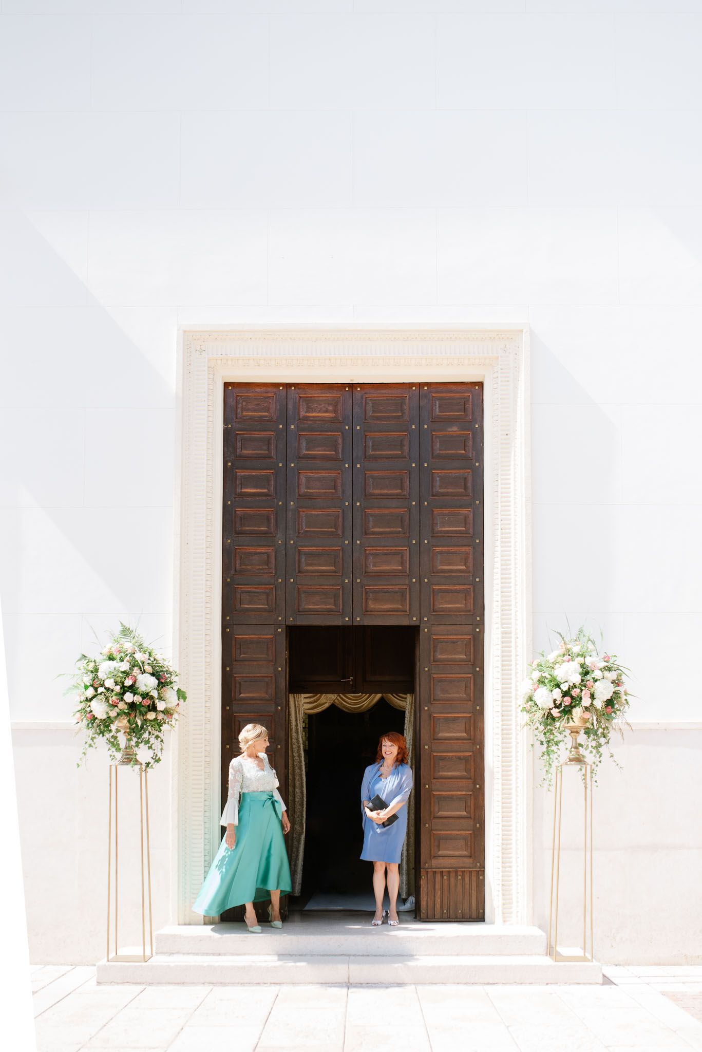 Large wooden church doors with flower arrangements on pedestals framing the entrance.