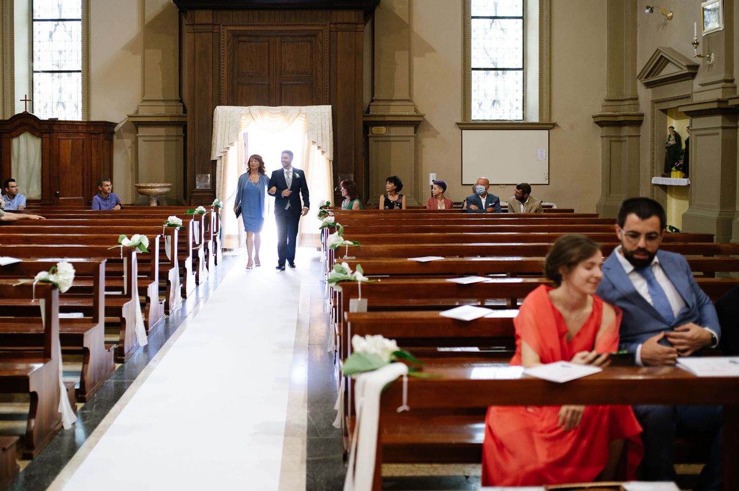 Traditional church interior with wooden pews and aisle runner during a wedding ceremony.