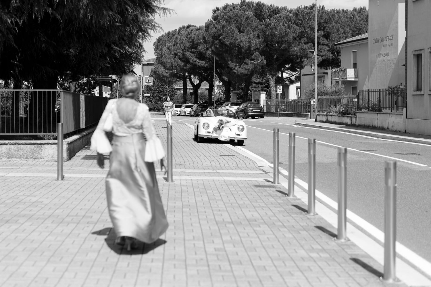 Black and white photo of a figure walking along a modern urban sidewalk with railings.