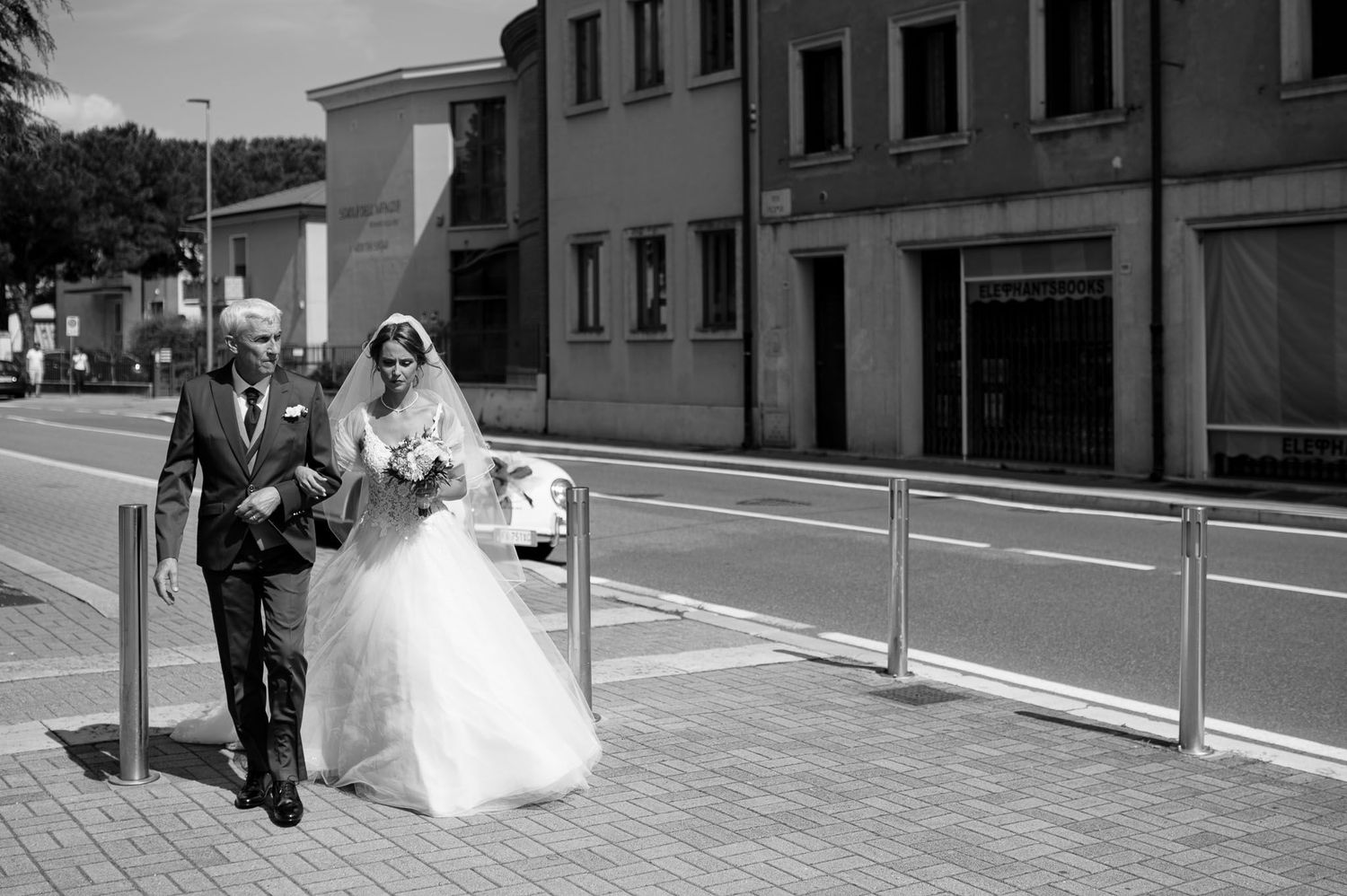 Black and white street scene of a couple walking along a sidewalk with metal railings.