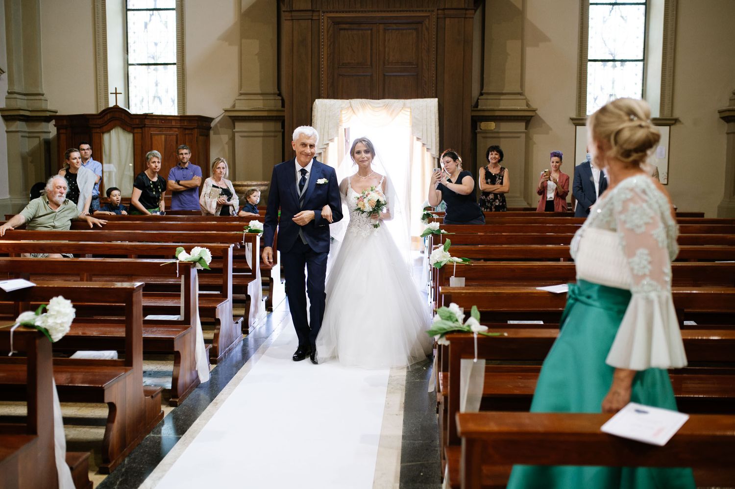 Traditional church wedding ceremony with guests seated in wooden pews and white aisle runner.