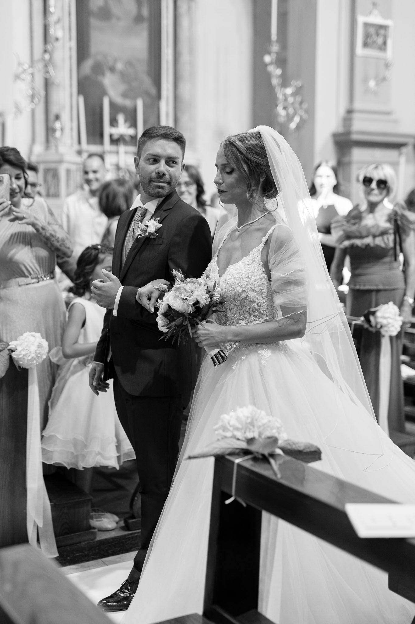 Elegant Catholic church wedding ceremony with couple at the altar surrounded by white floral arrangements and guests.