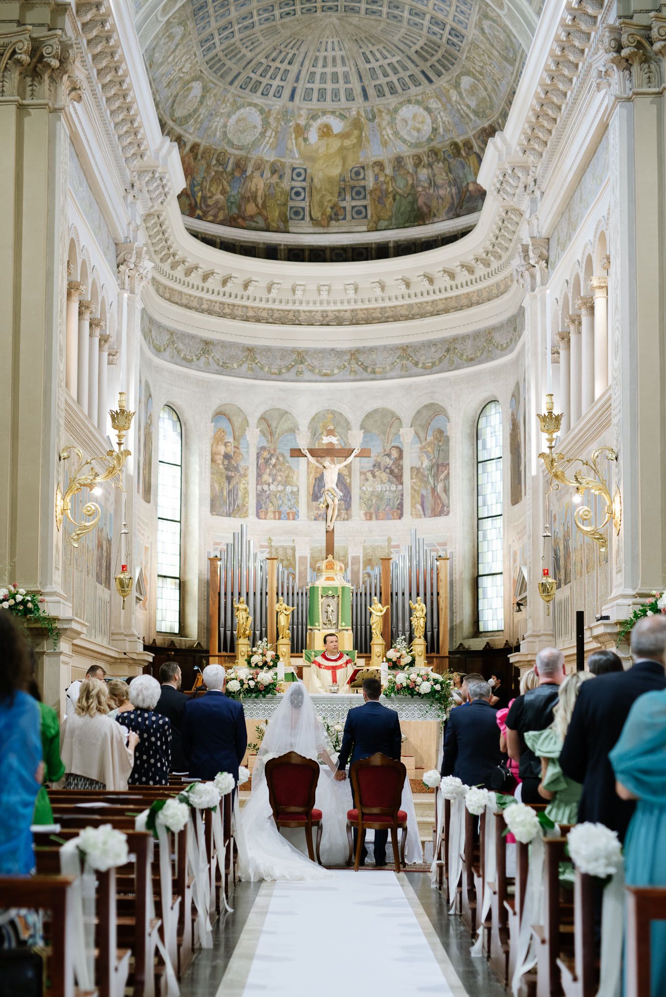 Beautiful baroque cathedral interior with ornate dome ceiling, organ pipes and white floral altar decorations.