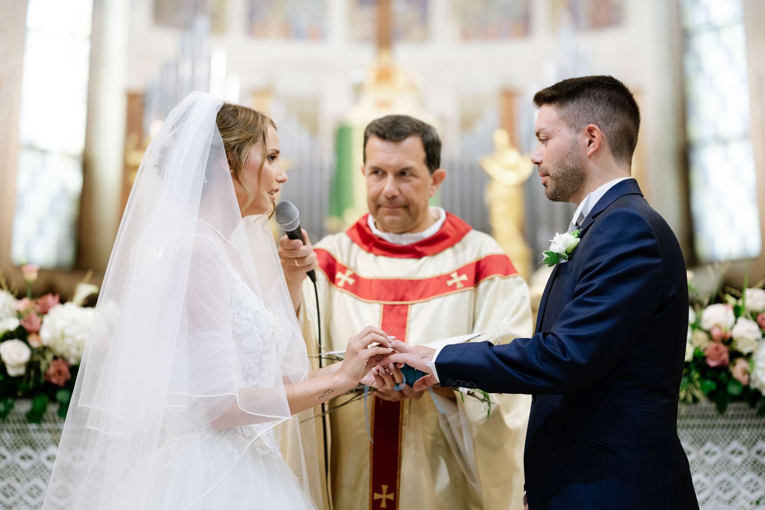 Wedding ceremony in progress with priest in red stole conducting traditional Catholic marriage rites.