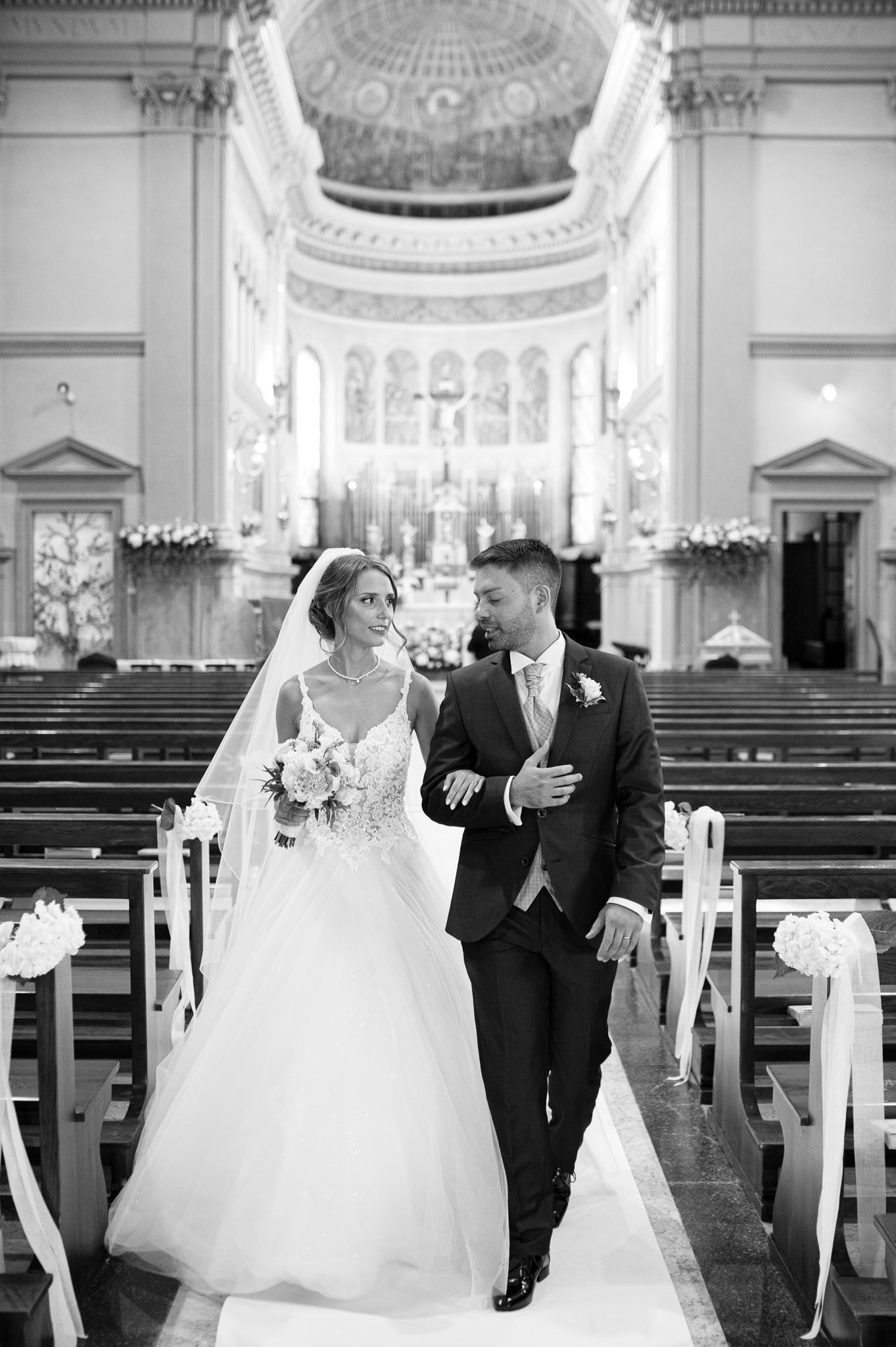 A couple walks down the church aisle after their wedding ceremony in black and white.