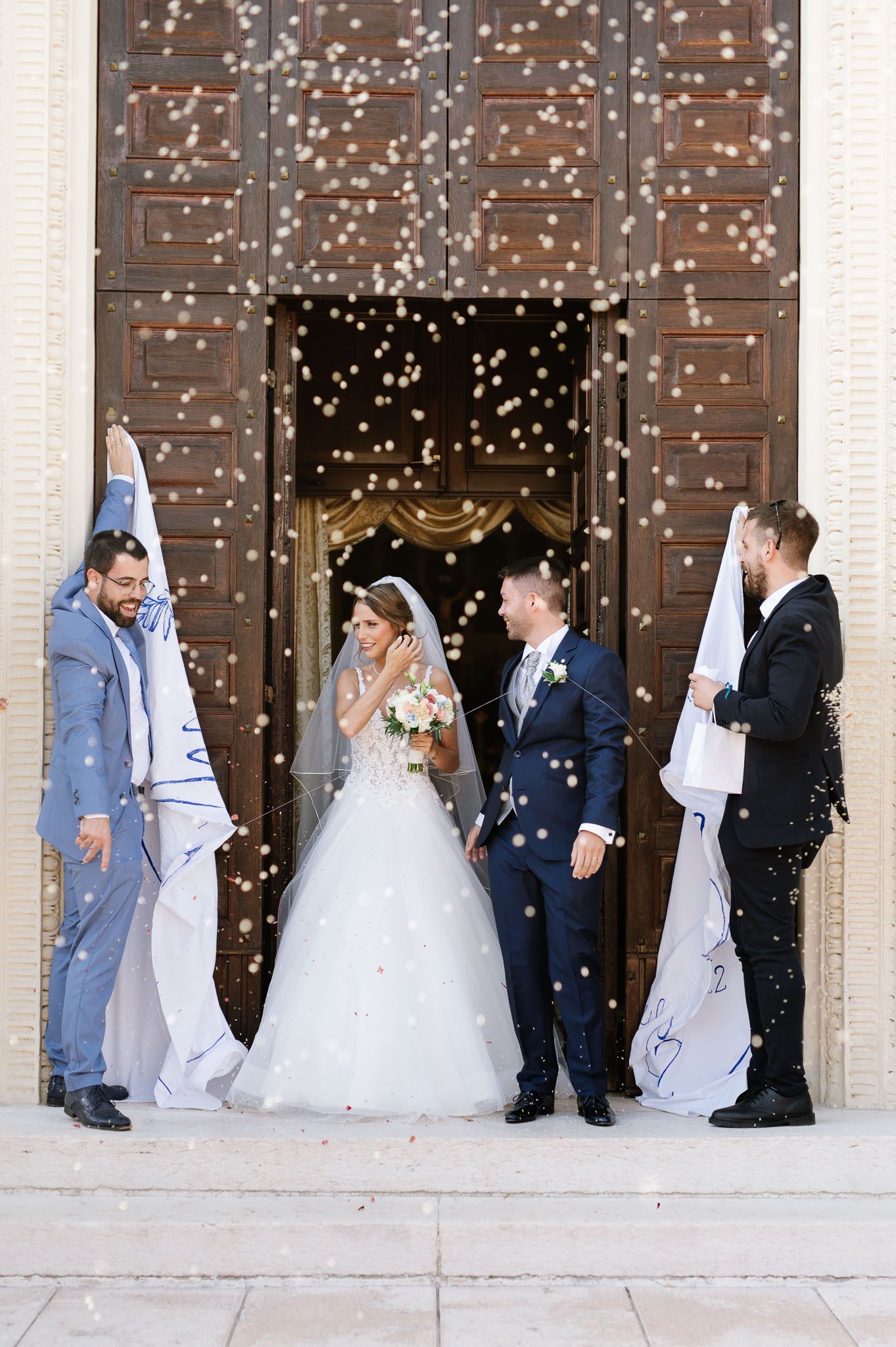 Wedding party celebrates with confetti outside large wooden church doors.