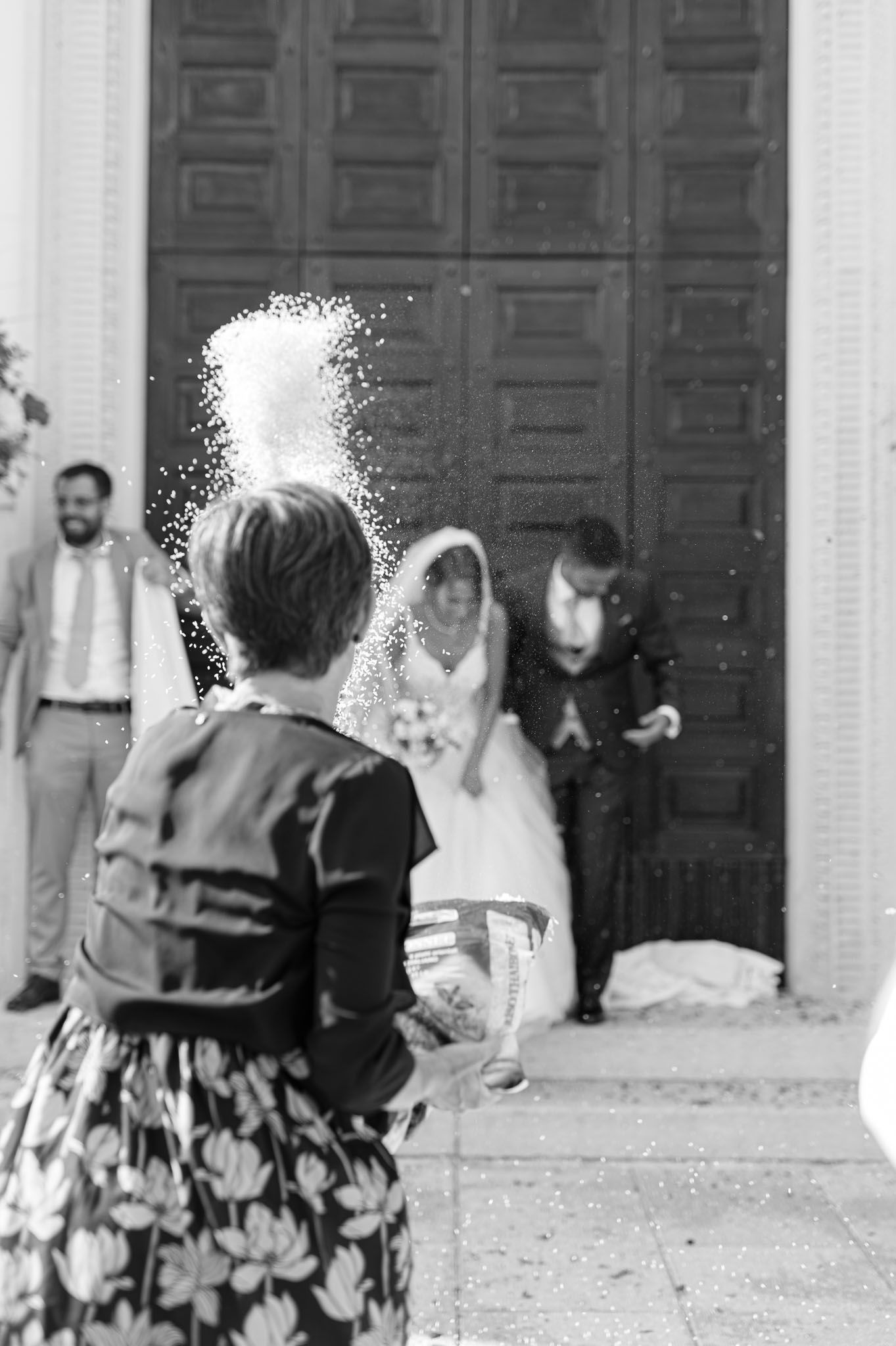 Black and white photo of guests throwing confetti at newlyweds outside church doors.
