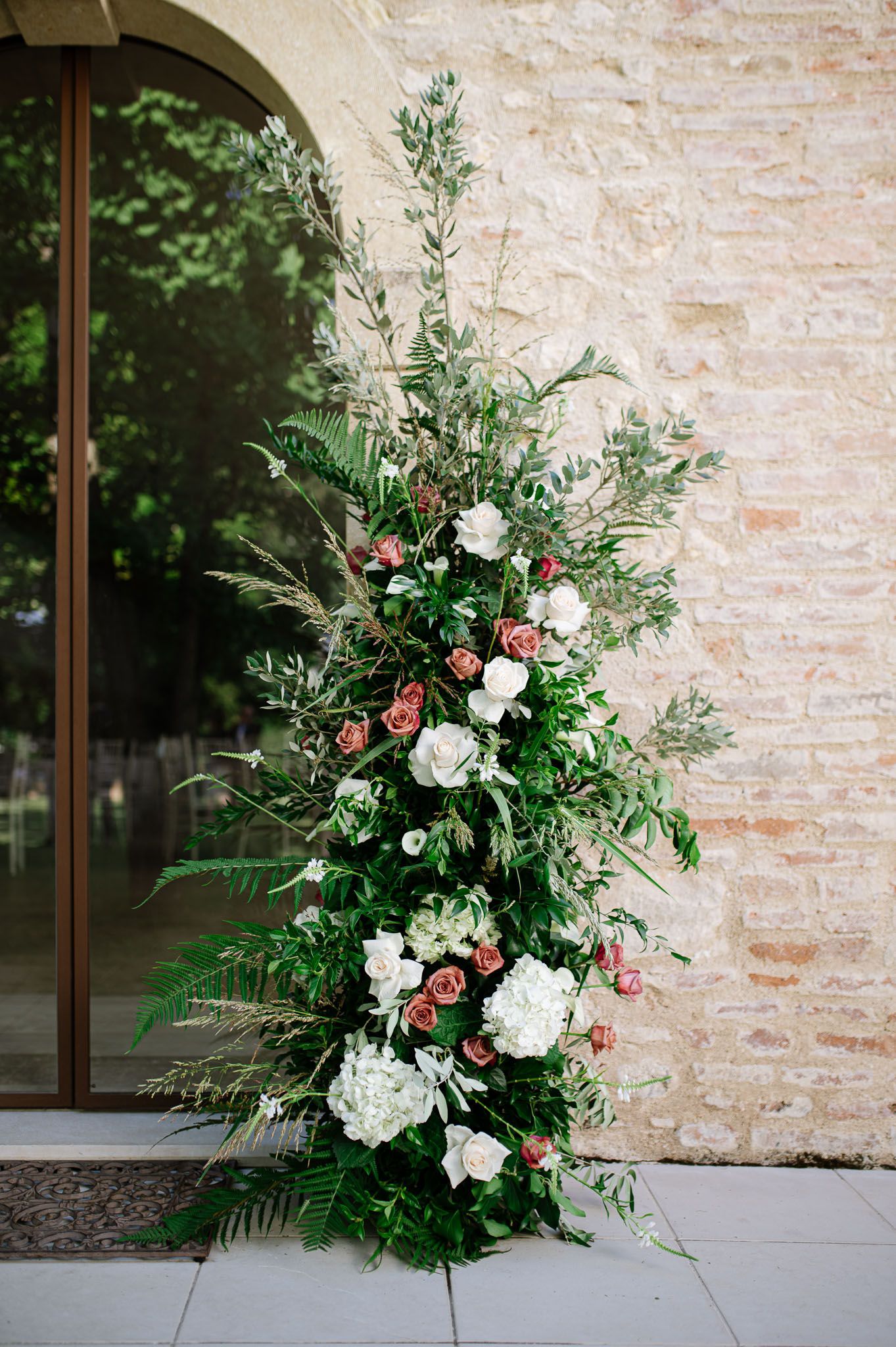 Elegant floral arrangement with white roses and greenery against a stone wall.