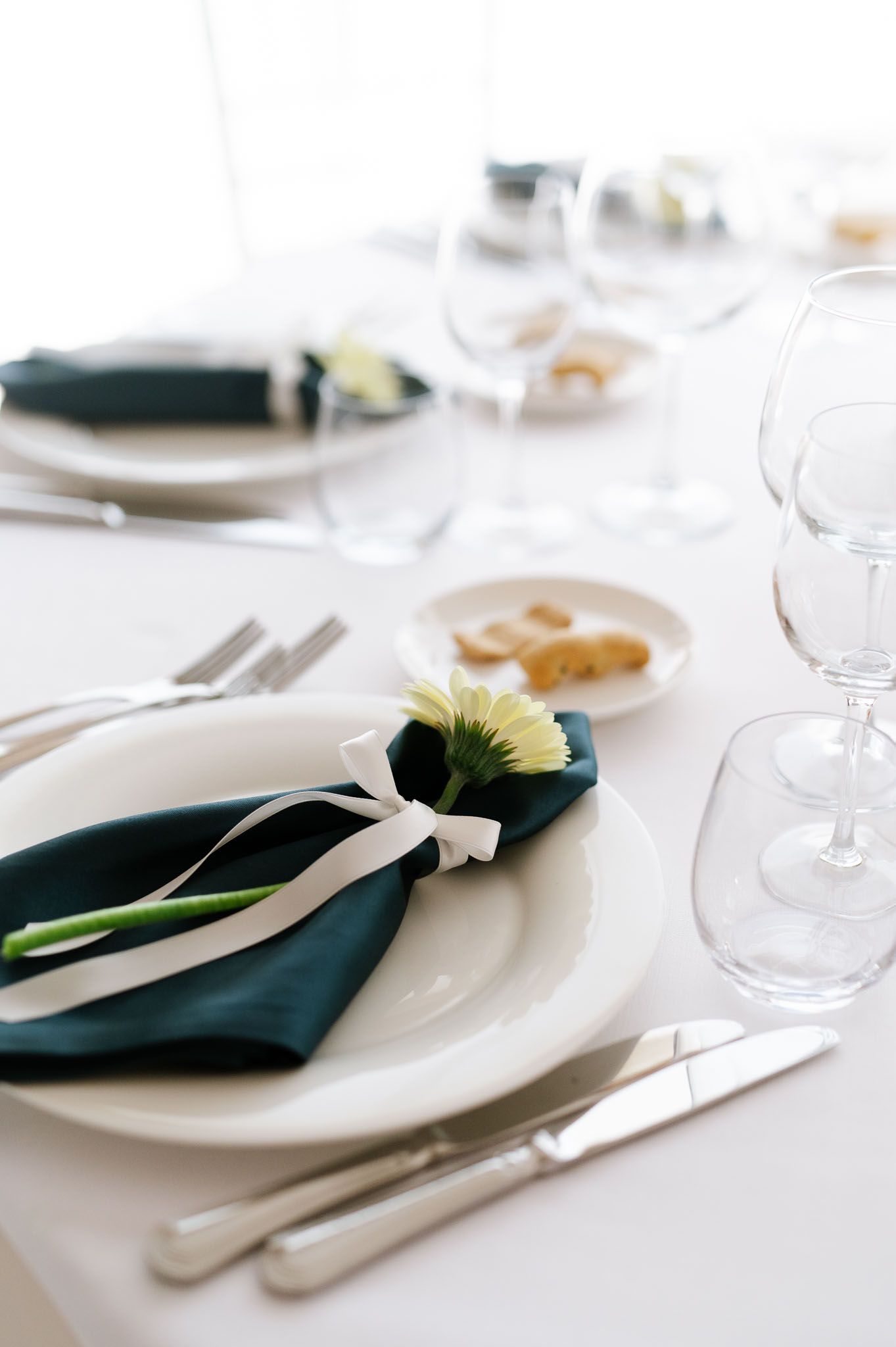 Formal place setting with white plates, teal napkin, and flower decoration on white tablecloth.