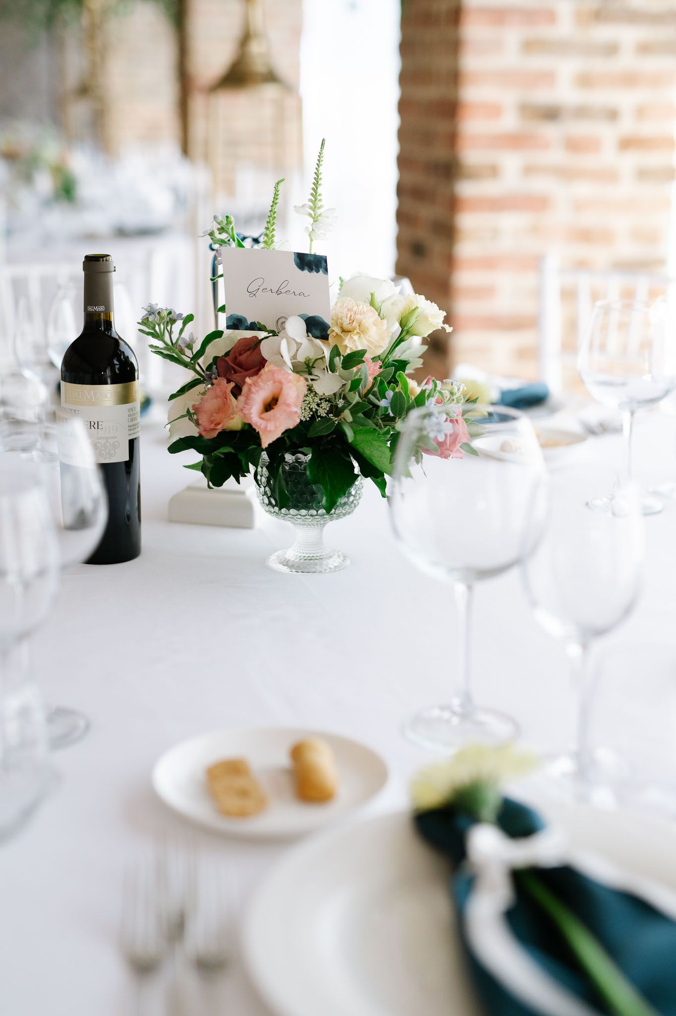 Wedding table setting with white linens, wine glasses and pink floral centerpiece.