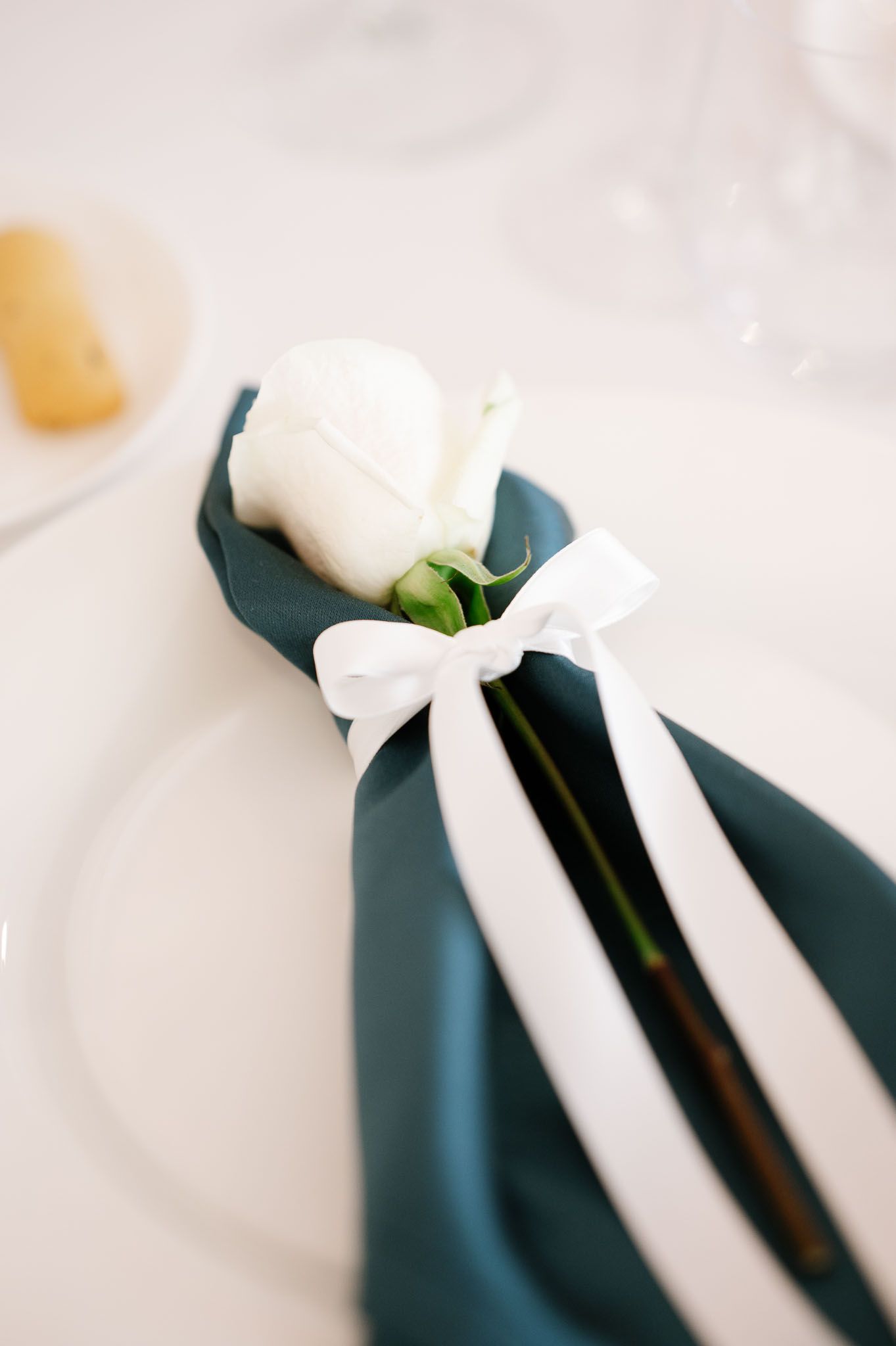 A white rose and bow decorate a navy blue napkin in an elegant table setting.