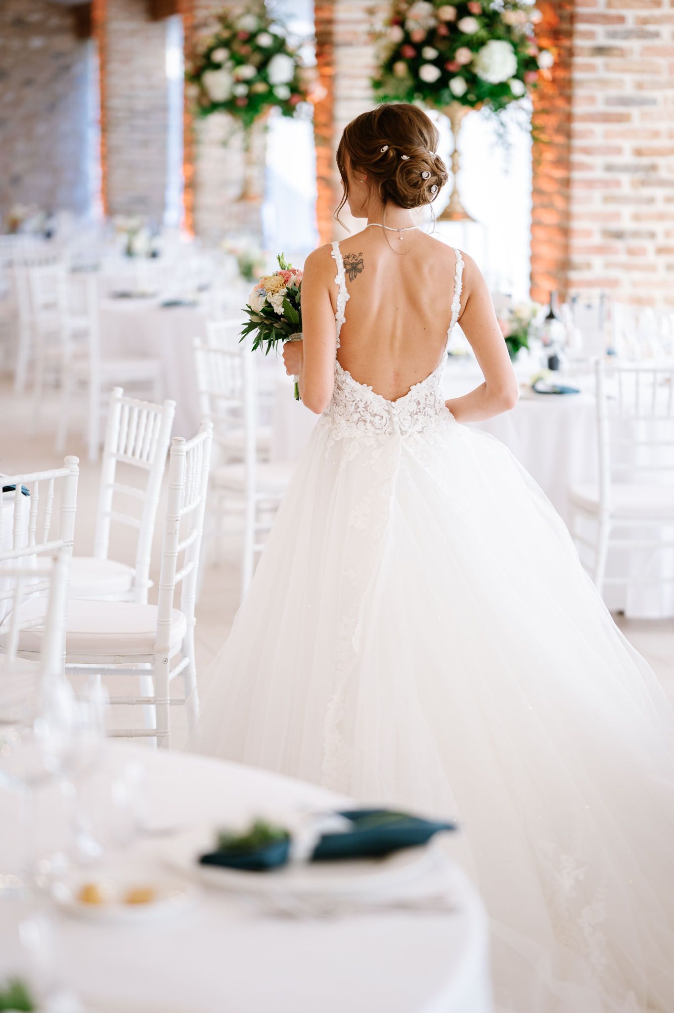Back view of wedding dress showing low-cut lace detail in a white reception venue.