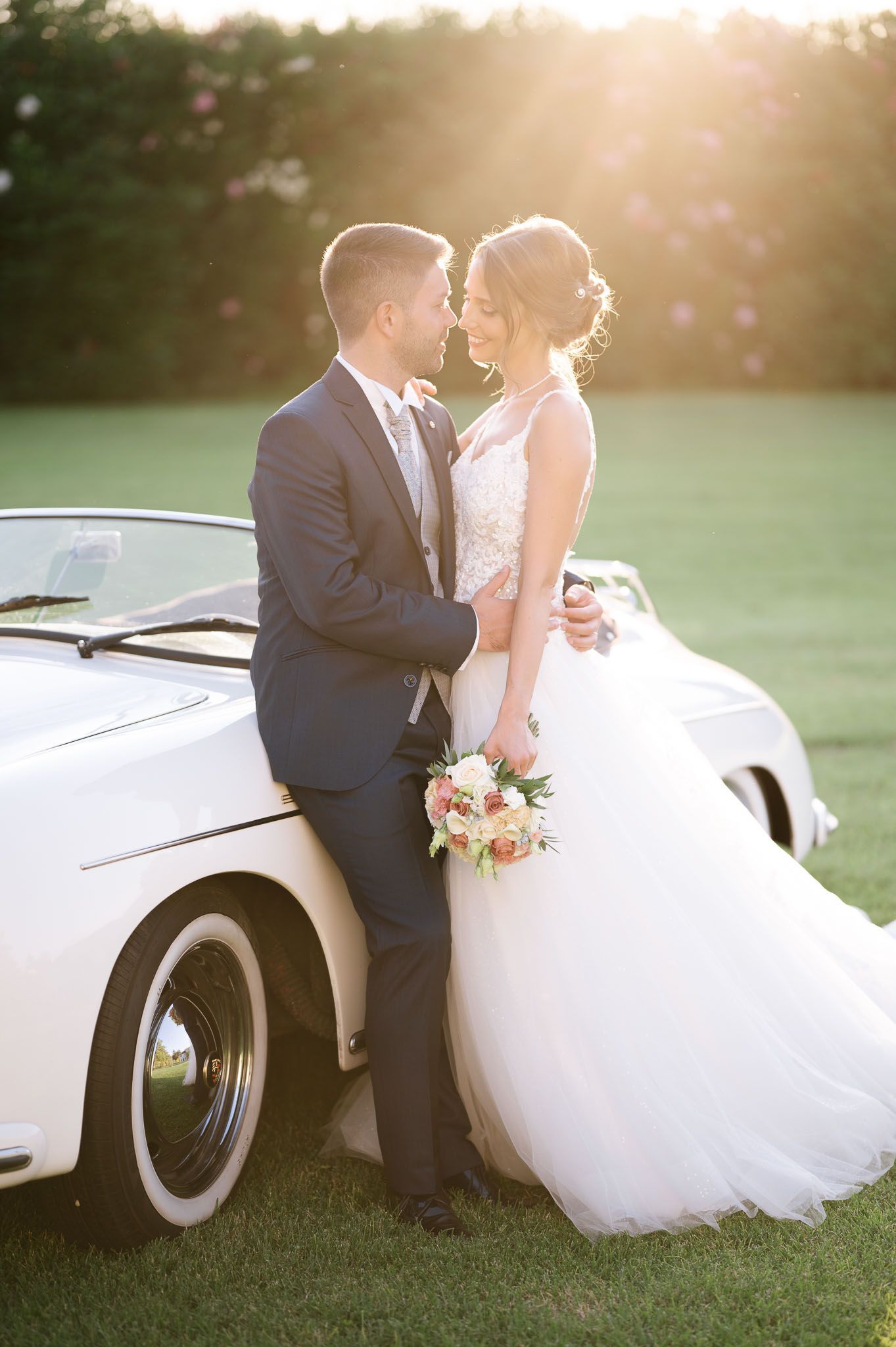 Romantic wedding portrait with couple leaning against classic white car.