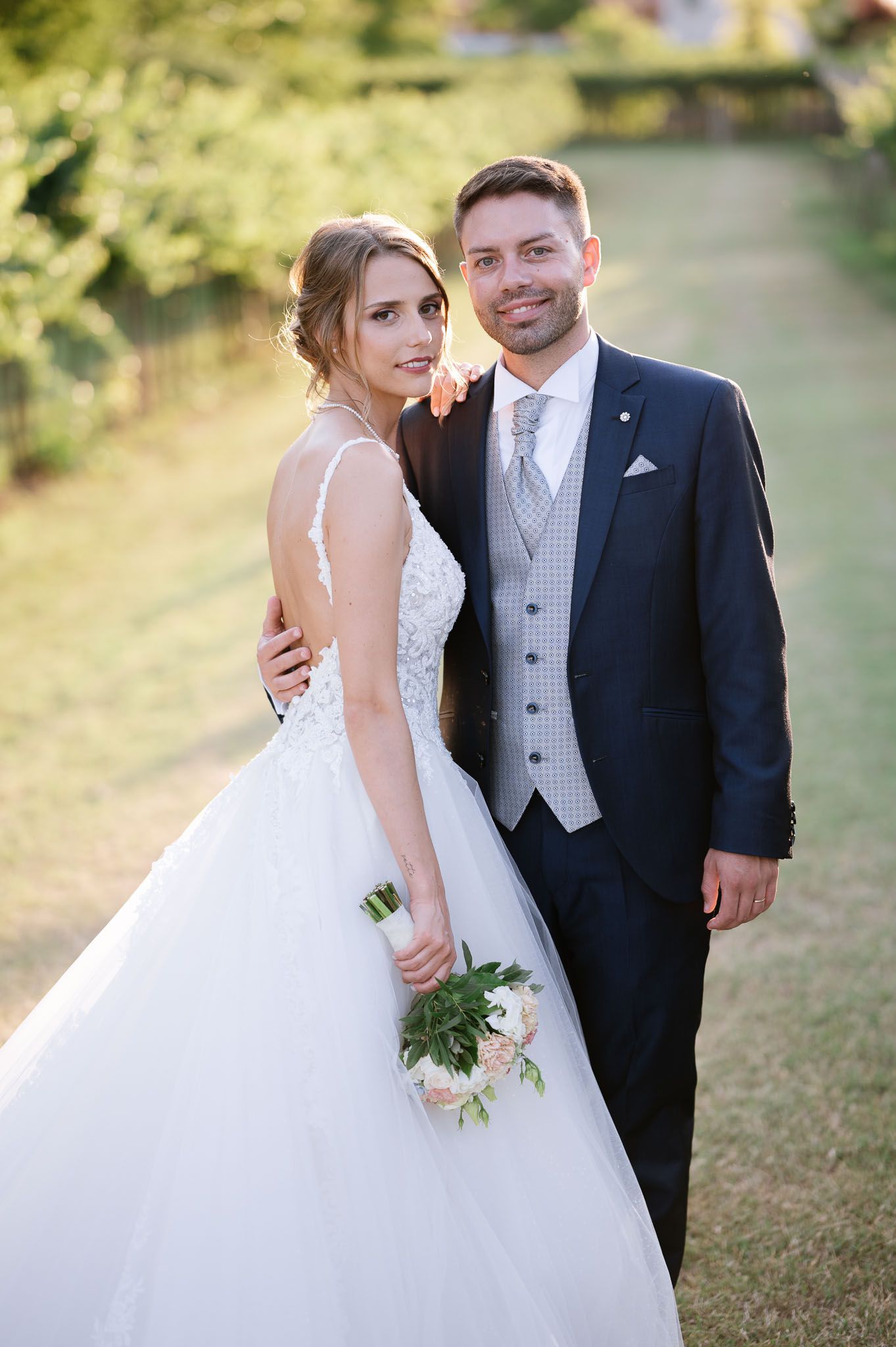 Elegant wedding portrait of couple in formal attire against nature backdrop.