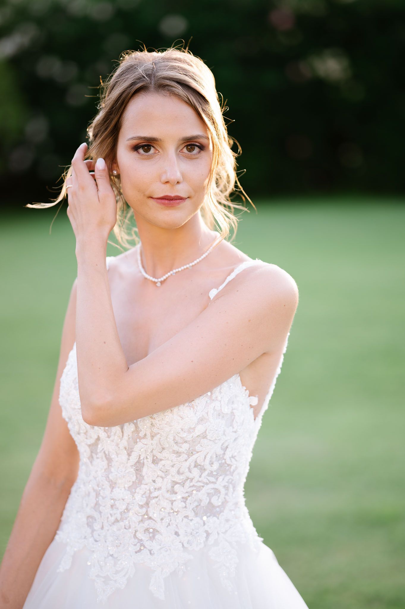 A portrait of a bride wearing a strapless lace wedding gown and delicate necklace in golden sunlight.