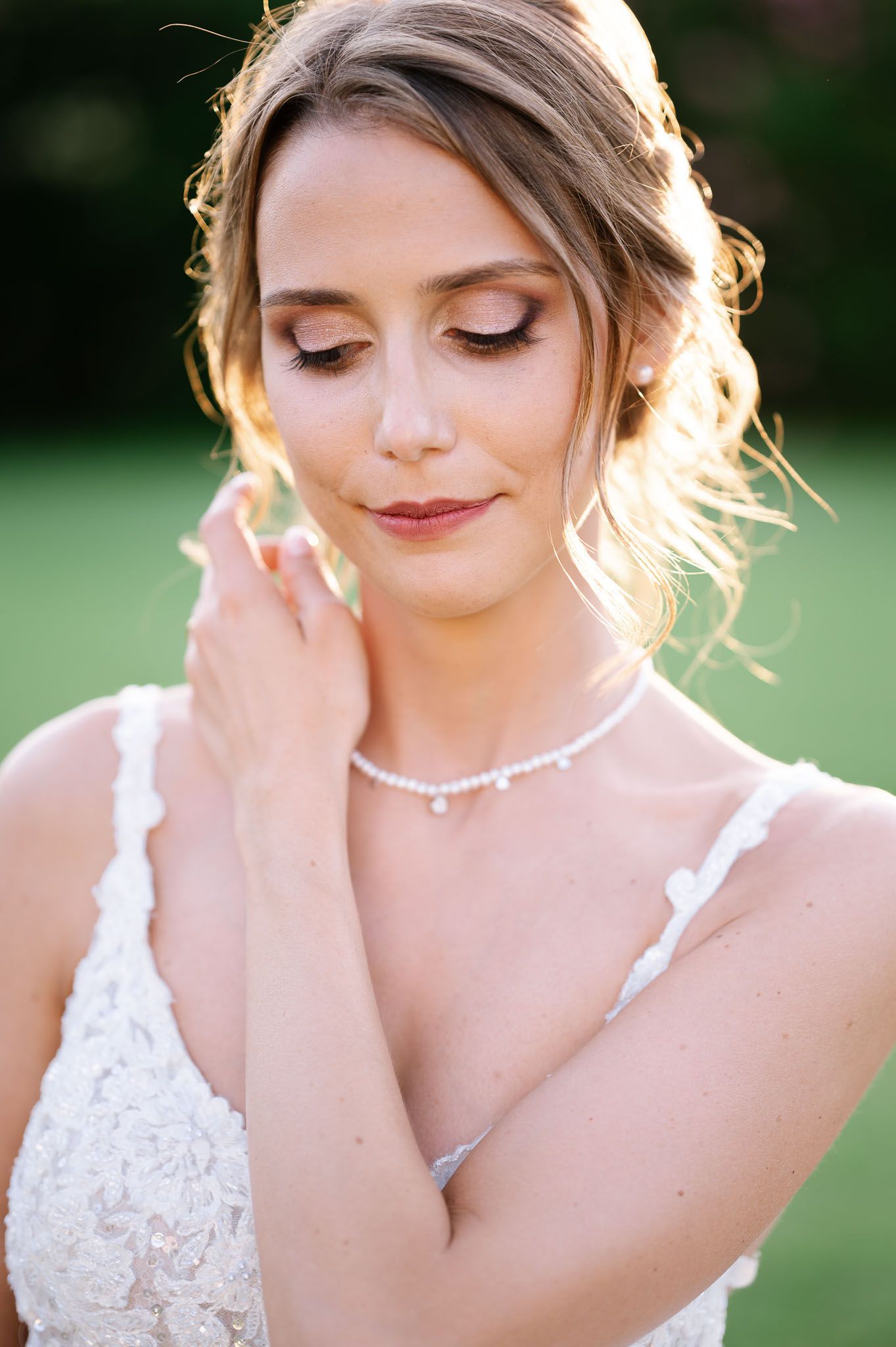 A close-up bridal portrait showing delicate makeup and jewelry in warm evening light.