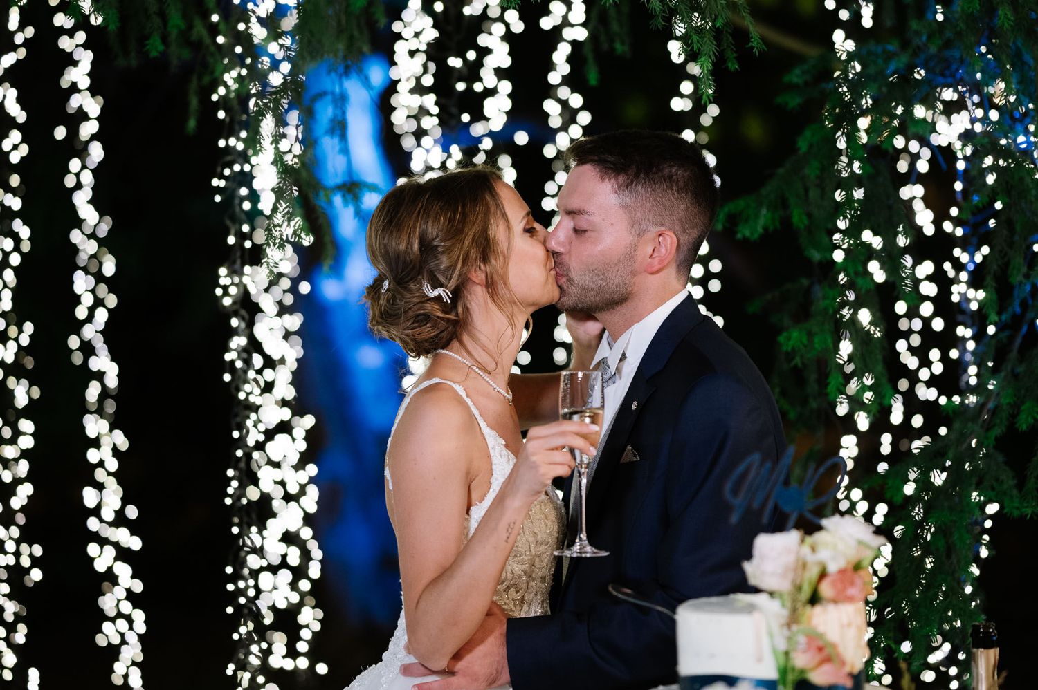 Romantic moment shared beside a wedding cake under cascading fairy lights and greenery.