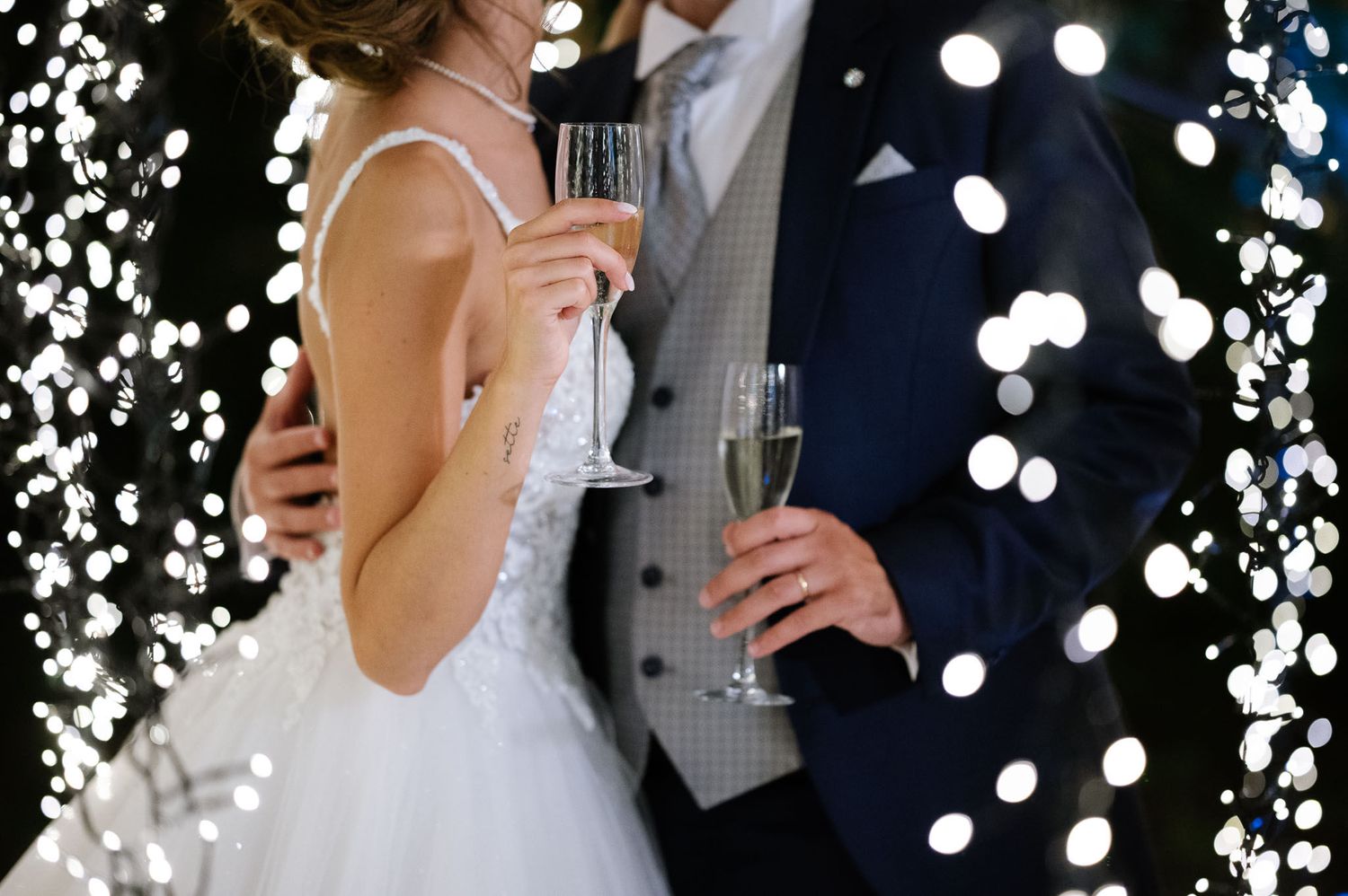 Close-up of champagne toast with string lights creating magical bokeh background.