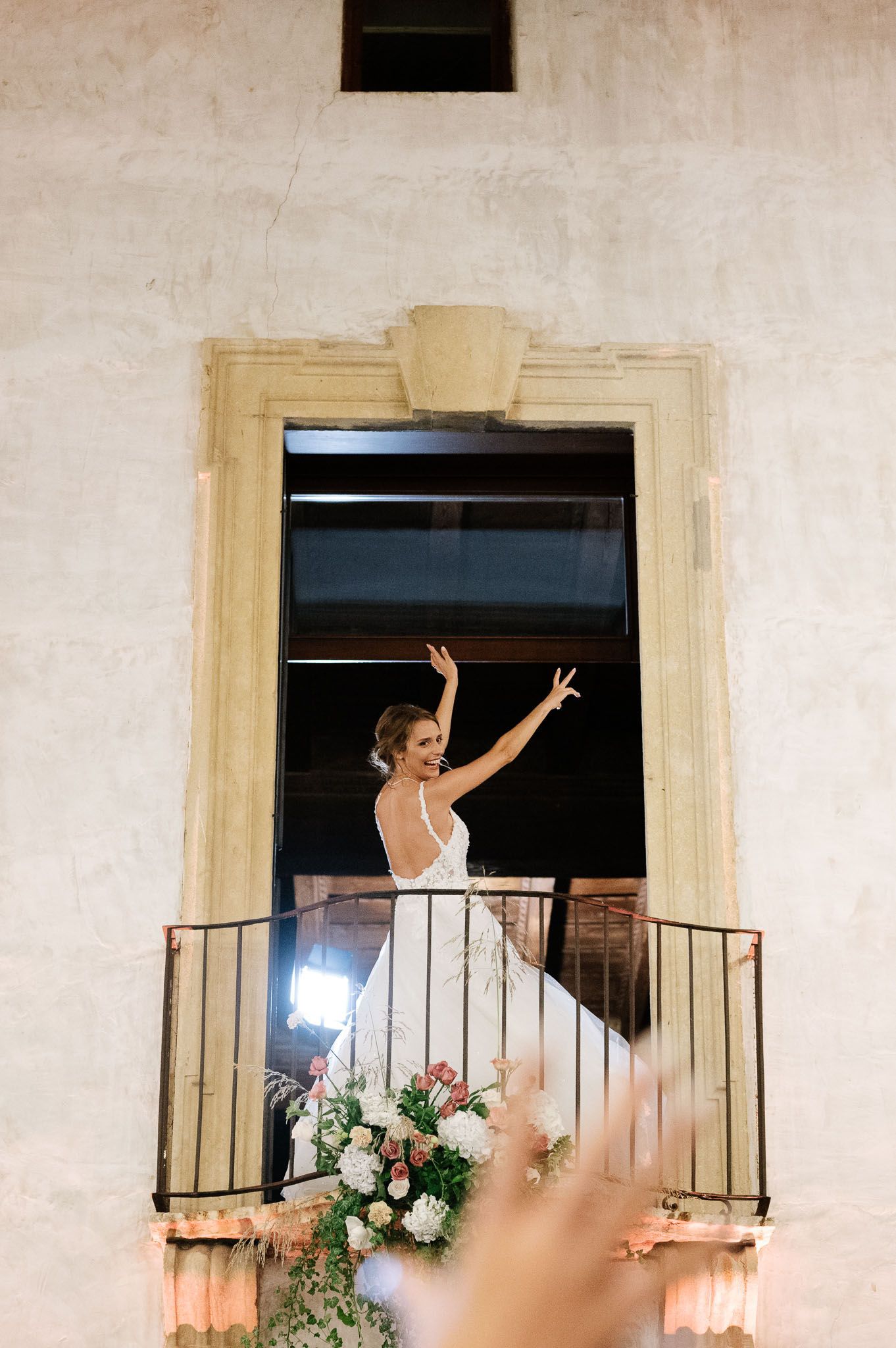 Elegant wedding scene with excited figure waving from a flower-decorated balcony at a villa.