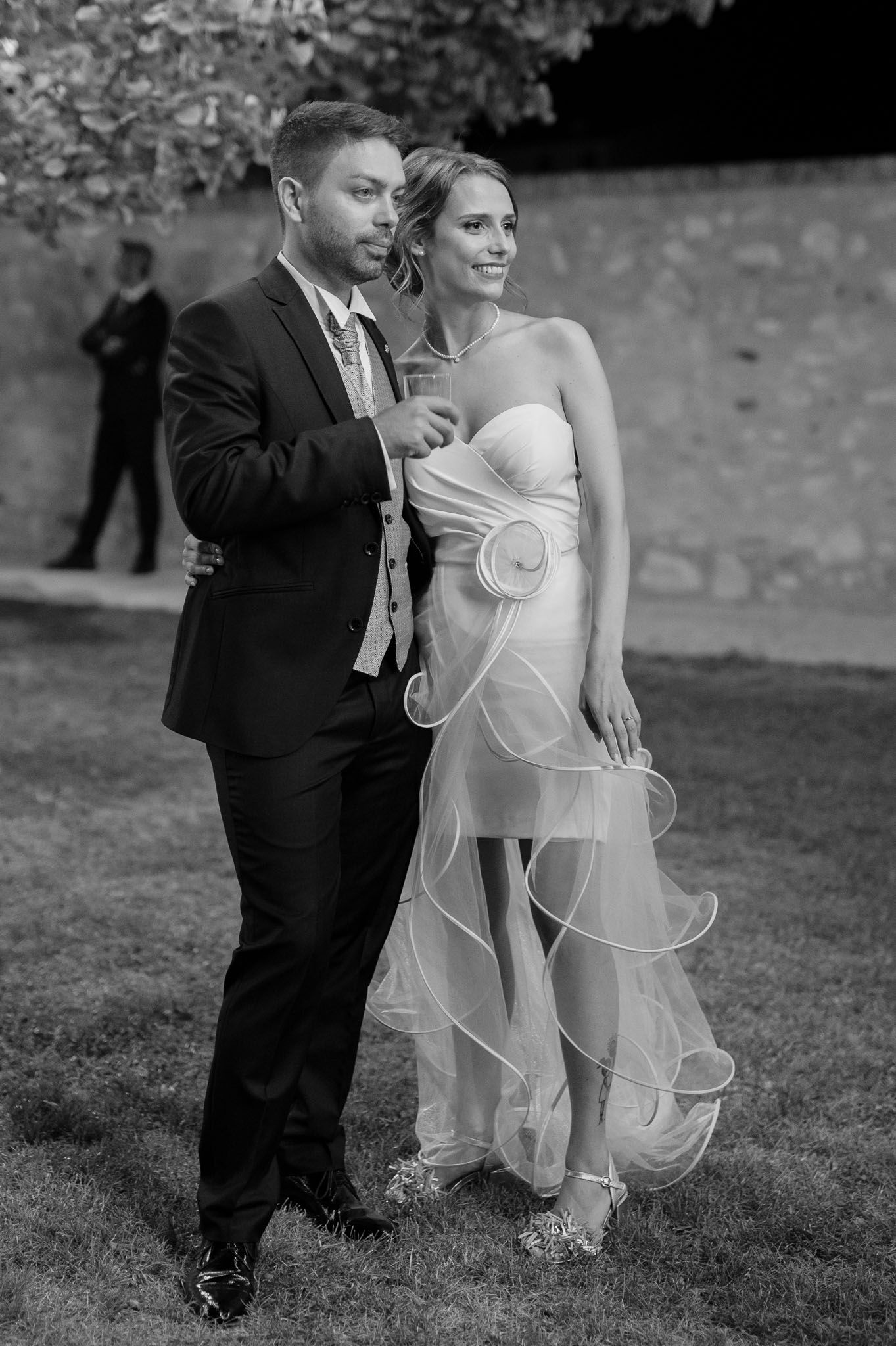 Elegant wedding couple poses outdoors against a stone wall in black and white photography.