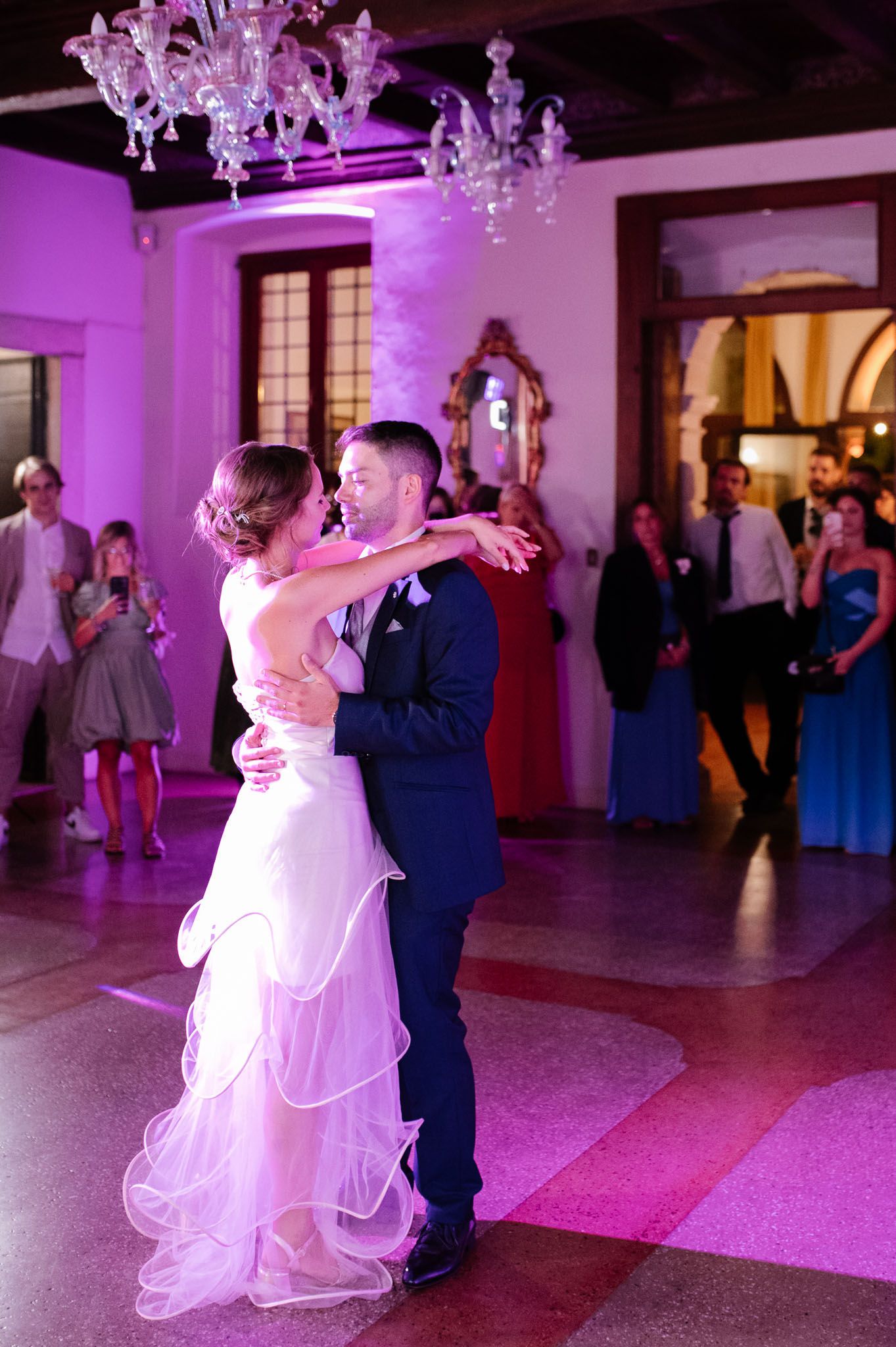 Romantic first dance under crystal chandeliers with purple lighting in an elegant ballroom.