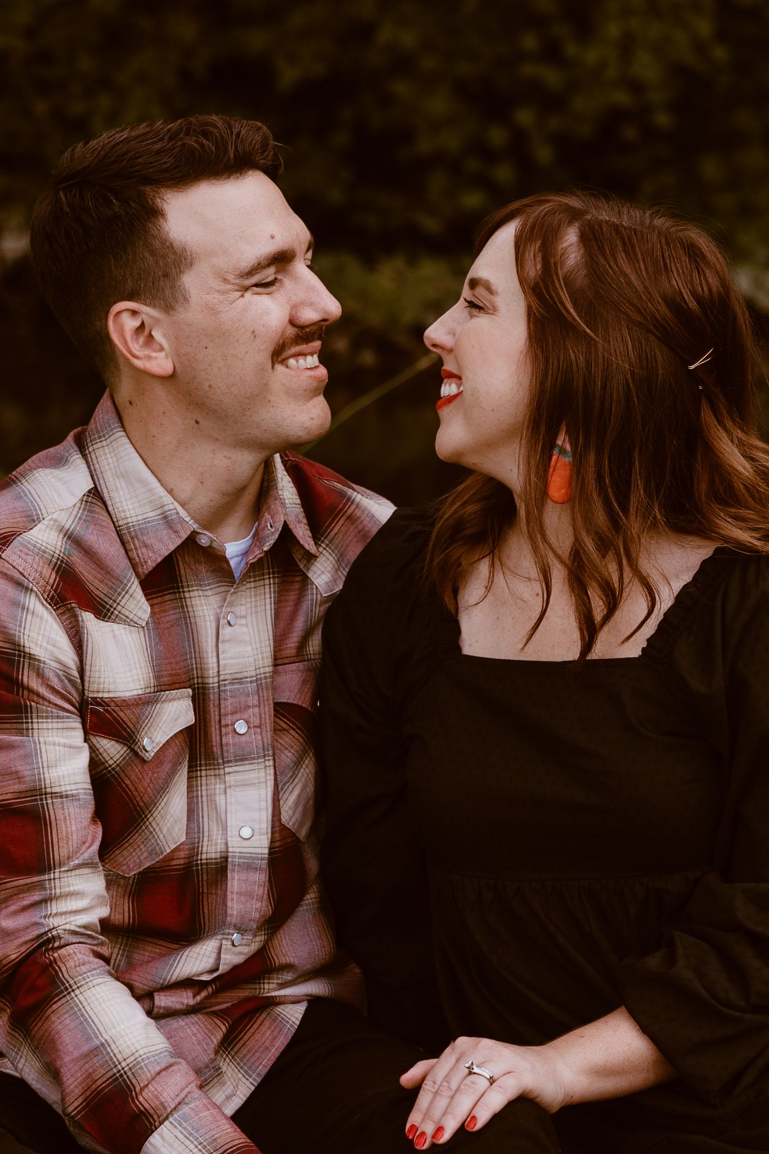 Couple laughing together outdoors wearing plaid and black clothing.