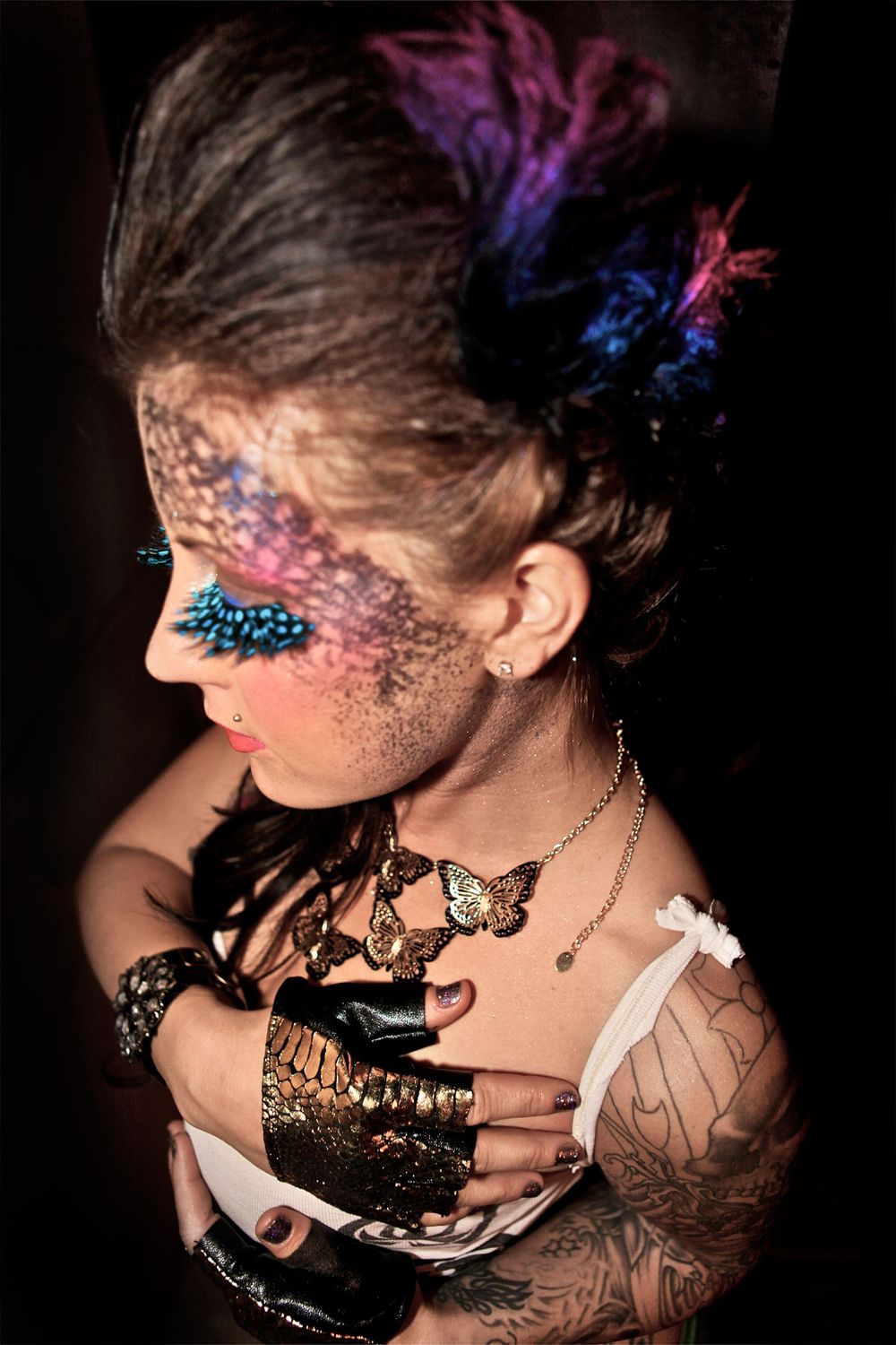 Creative makeup look featuring colorful face art with butterfly accessories and vibrant hair.