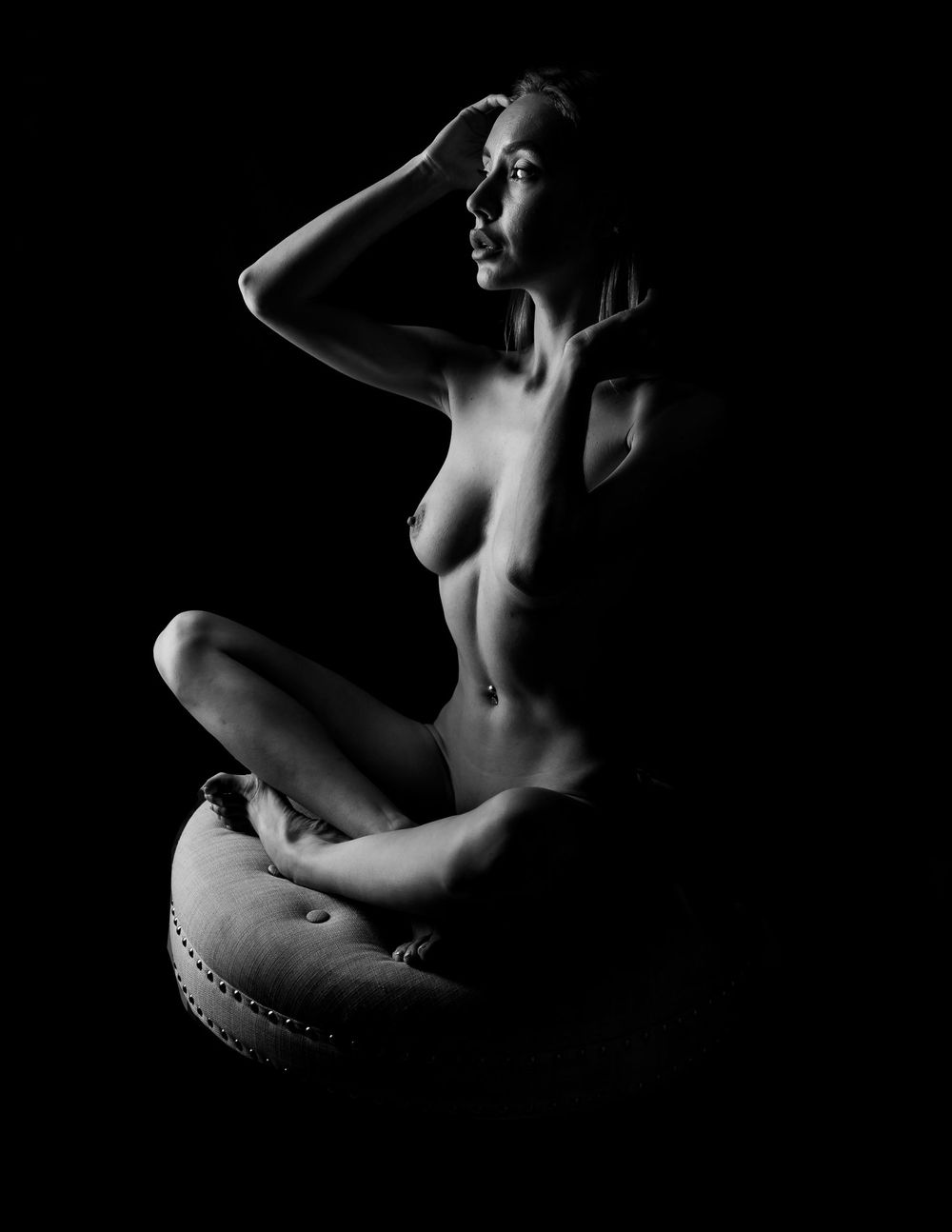Artistic black and white nude figure study with dramatic lighting and shadows on dark background.