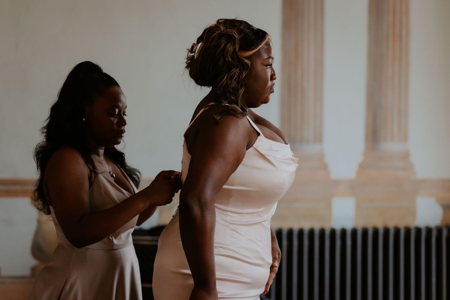 Intimate getting ready moment as bridesmaid helps with final wedding preparations.