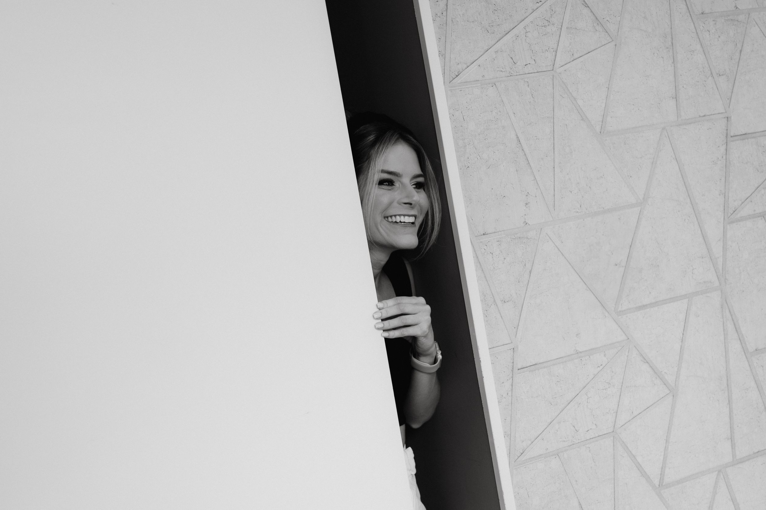 A black and white photo of someone peeking through a narrow opening with a playful expression.