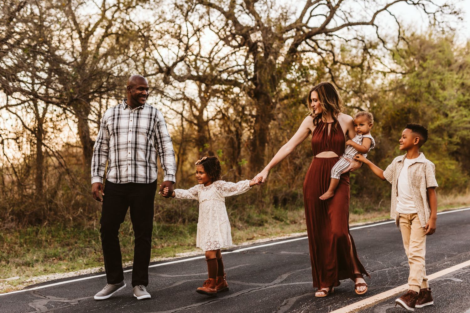 Family walking together and holding hands on a rural road at sunset.
