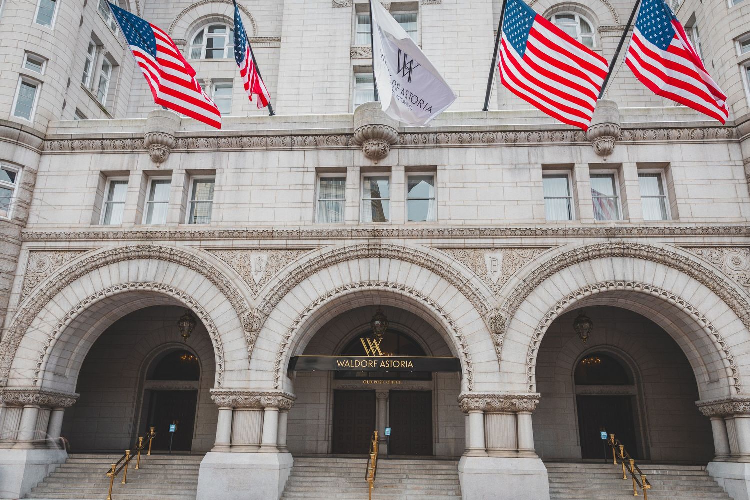 Historic building entrance with arched columns and American flags flying above at the Trump International Hotel.