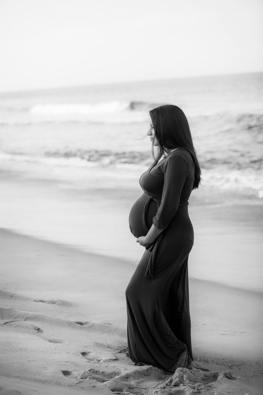 Black and white image of pregnant mom standing silhouette in dark dress.