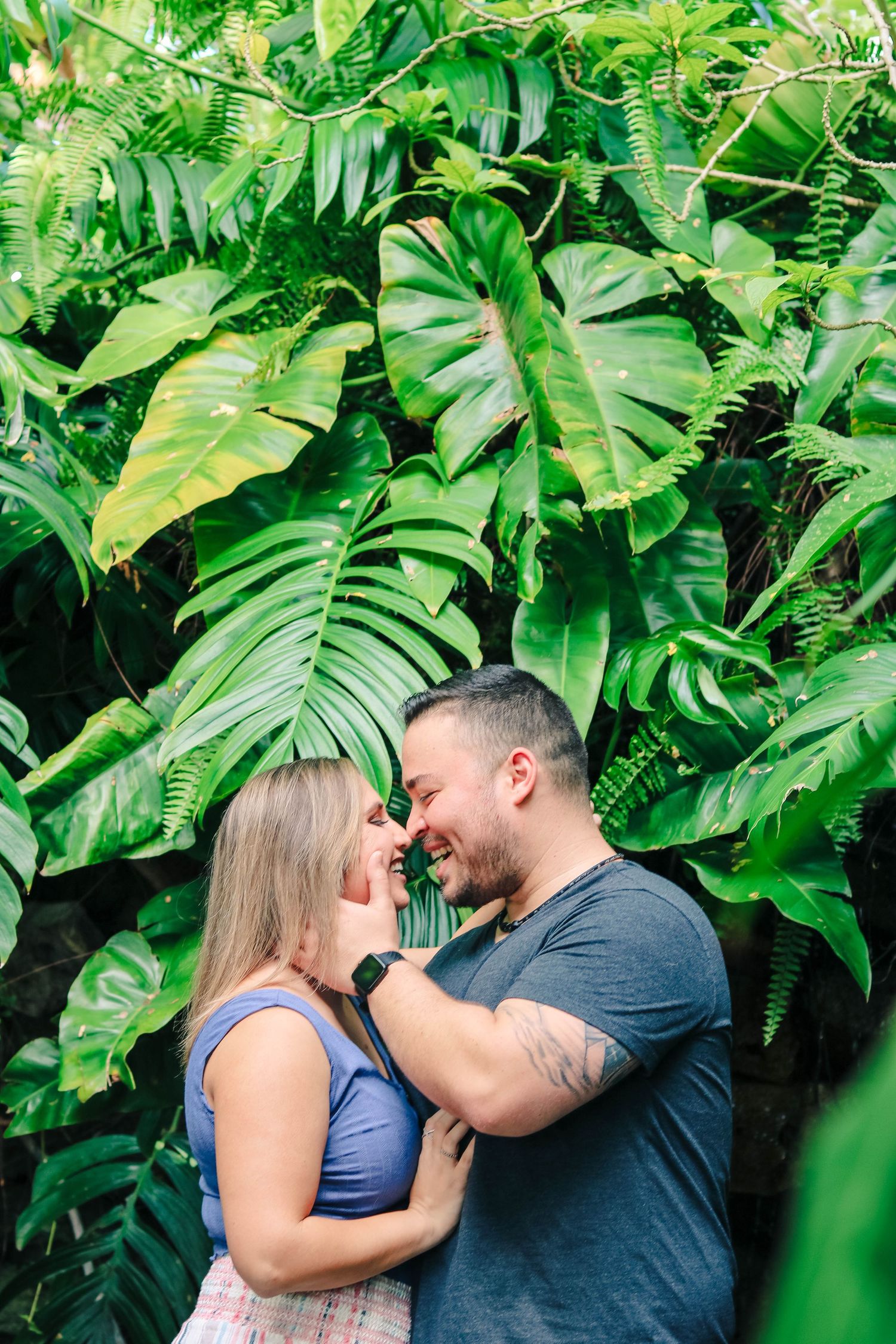 girl and boy nose kissing and smiling in front of greenery