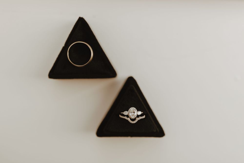 Diamond engagement ring and gold wedding band displayed in black triangular velvet ring boxes.