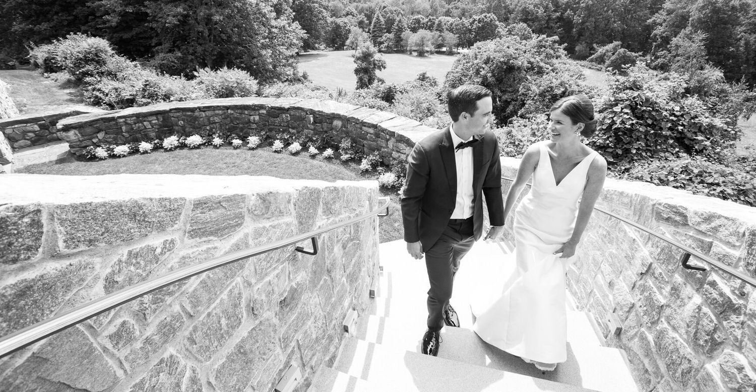Black and white shot of a couple descending stone steps in elegant wedding attire.
