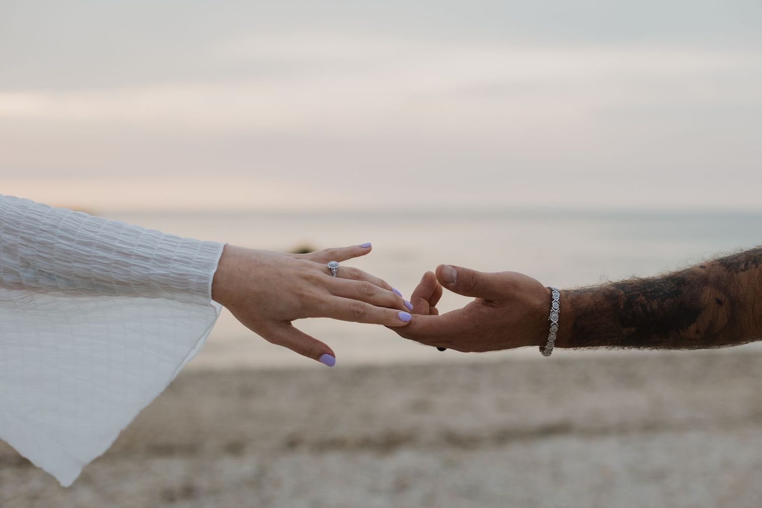 Close up of hands reaching towards each other against a beachy background.