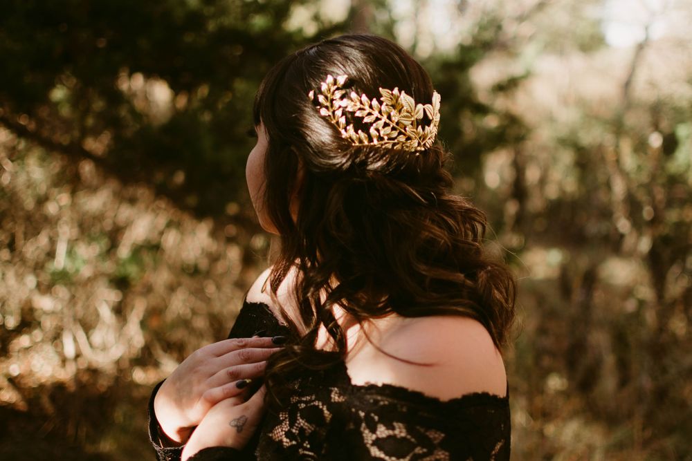 Elegant gold crown adorns dark wavy hair against black lace dress.