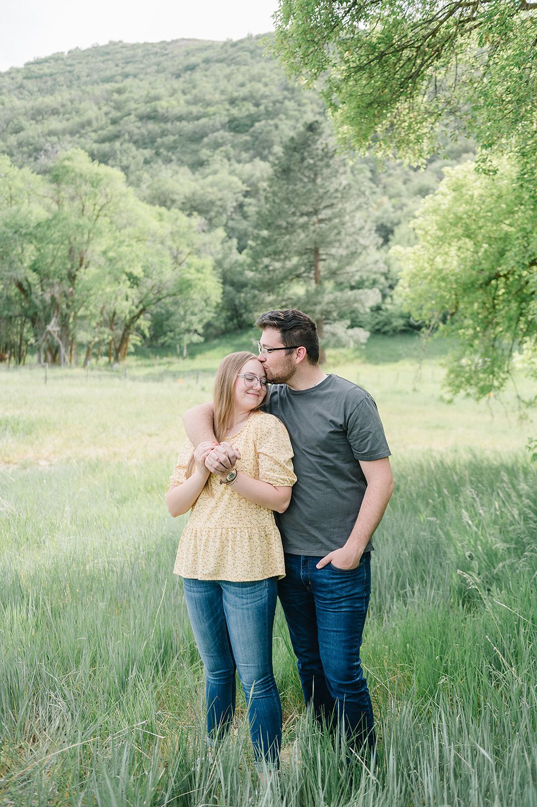 A tender moment shared between a couple in a lush green meadow surrounded by trees.