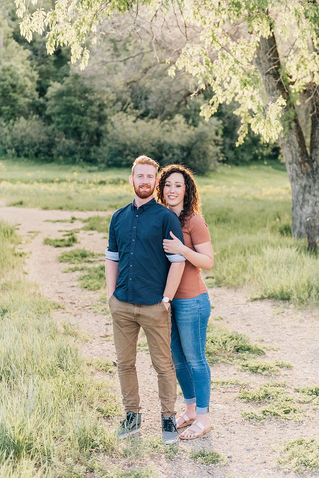 A sweet moment captured on a dirt path with sunlit trees in the background.