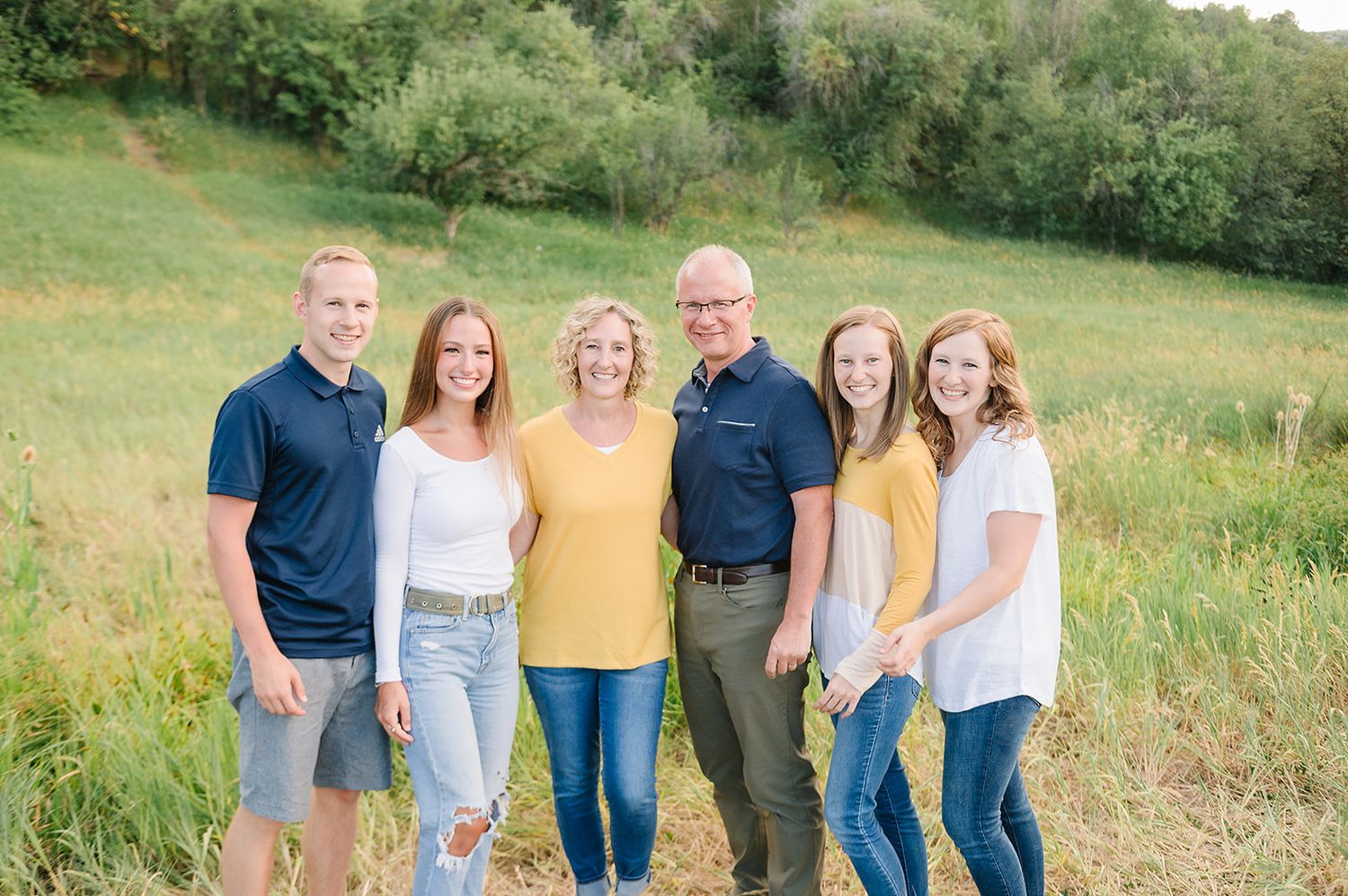 A group portrait of six people in coordinating outfits against a green hillside.