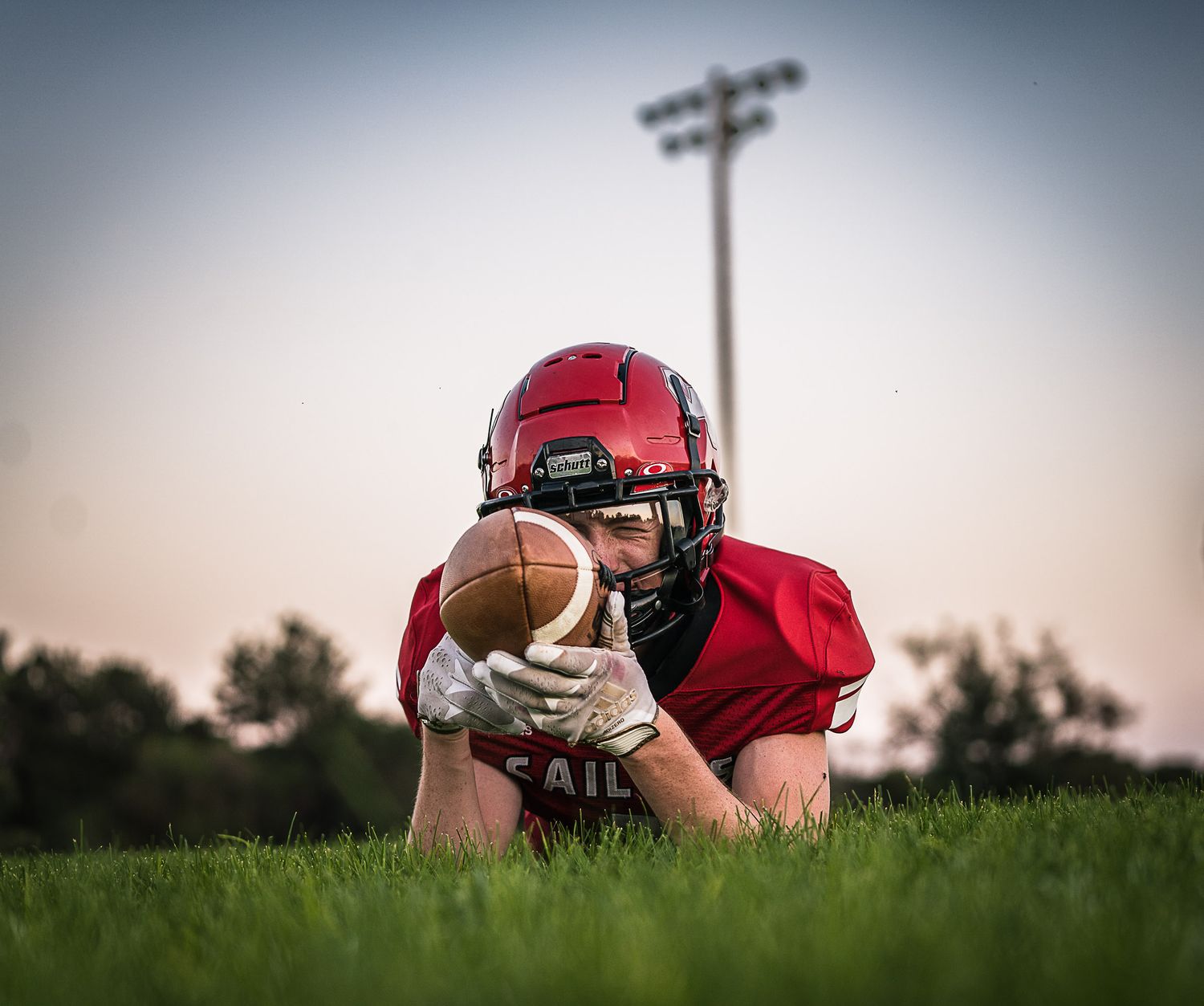 Football player lying in grass with ball during dramatic sunset sports photoshoot.
