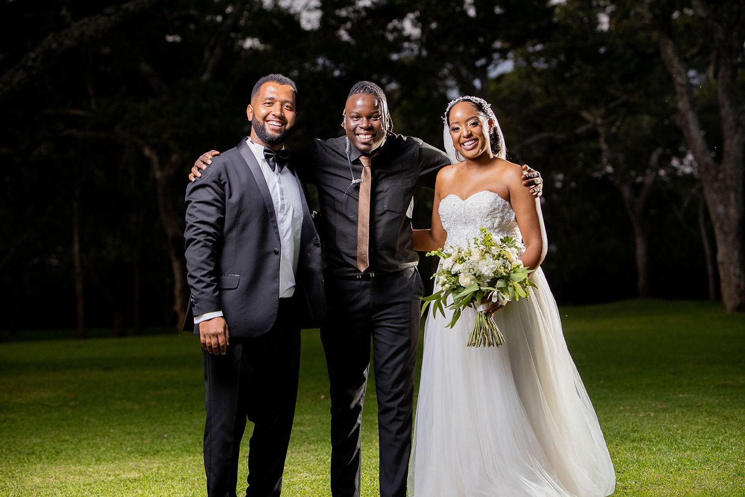 Wedding party poses outdoors on grassy lawn with bride holding bouquet.