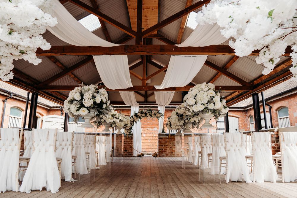 Elegant wedding venue with white floral arrangements and draped fabric decorating wooden beams.