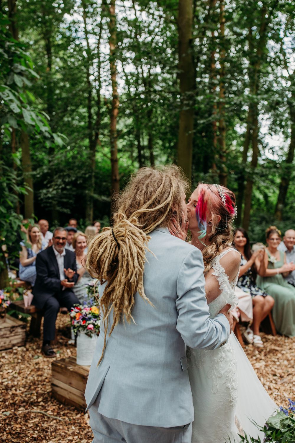 An intimate woodland wedding ceremony with guests seated among the trees.