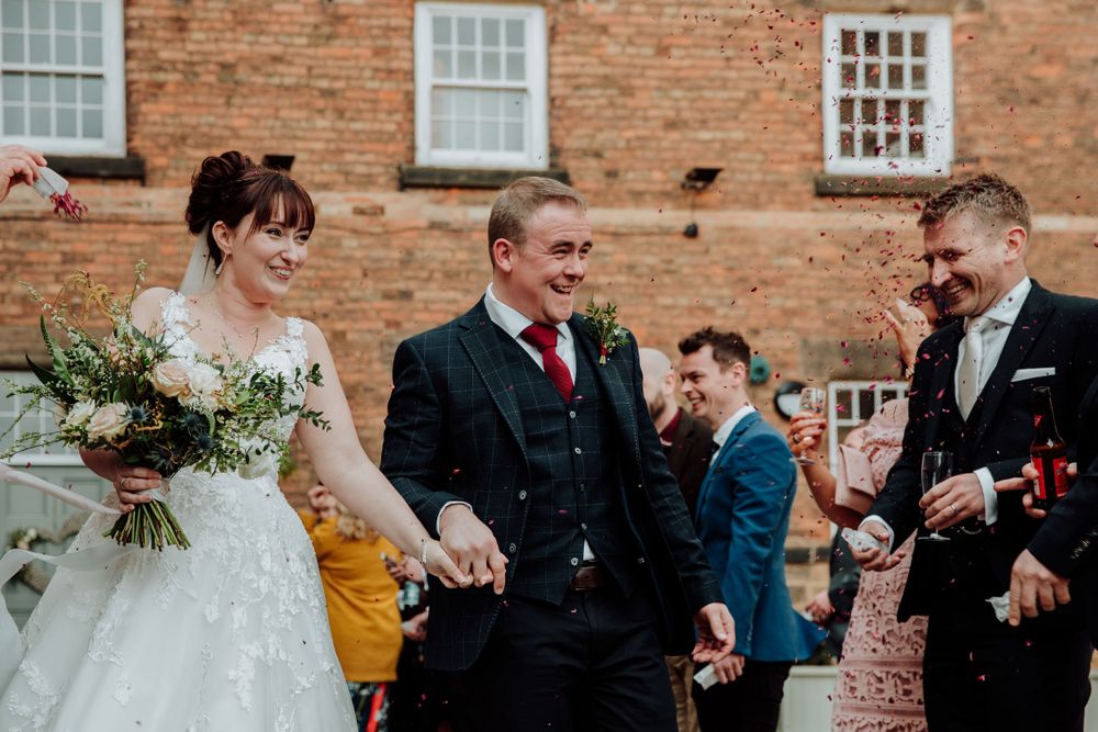 Wedding party shares laughter outside historic brick building during reception.