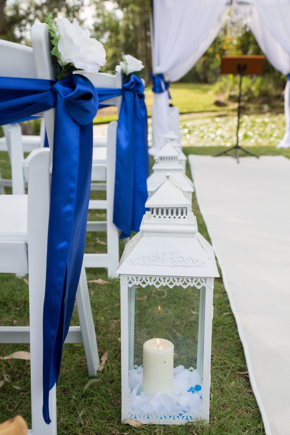 White decorative lanterns with blue ribbons line the outdoor wedding aisle.