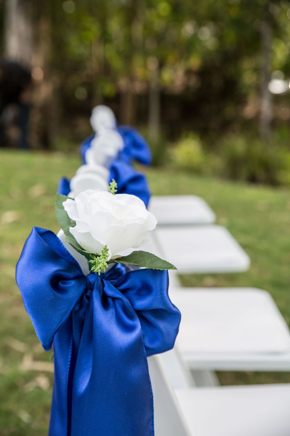 White folding chairs decorated with royal blue ribbon bows for an outdoor wedding ceremony.